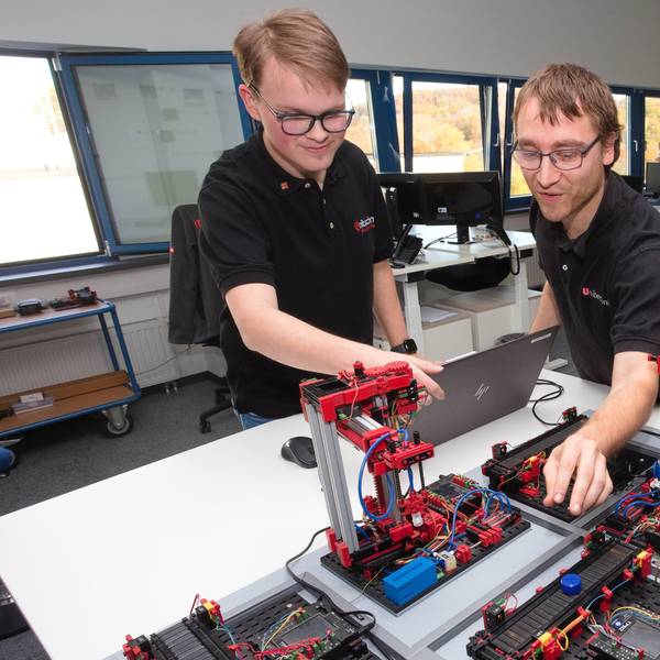 Zwei junge Männer fassen an eine Fischer-Technik-Anlage.