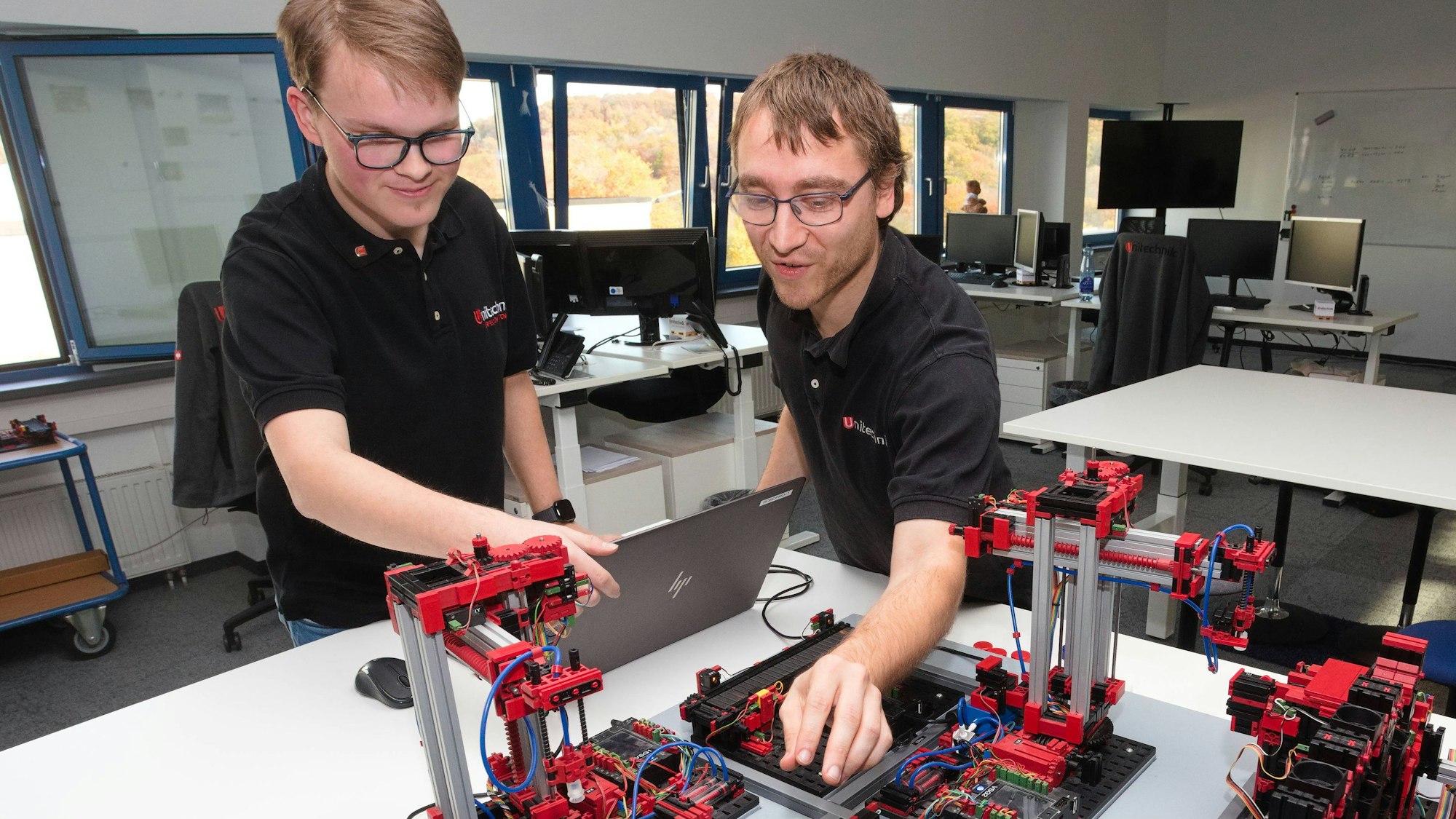 Zwei junge Männer fassen an eine Fischer-Technik-Anlage.