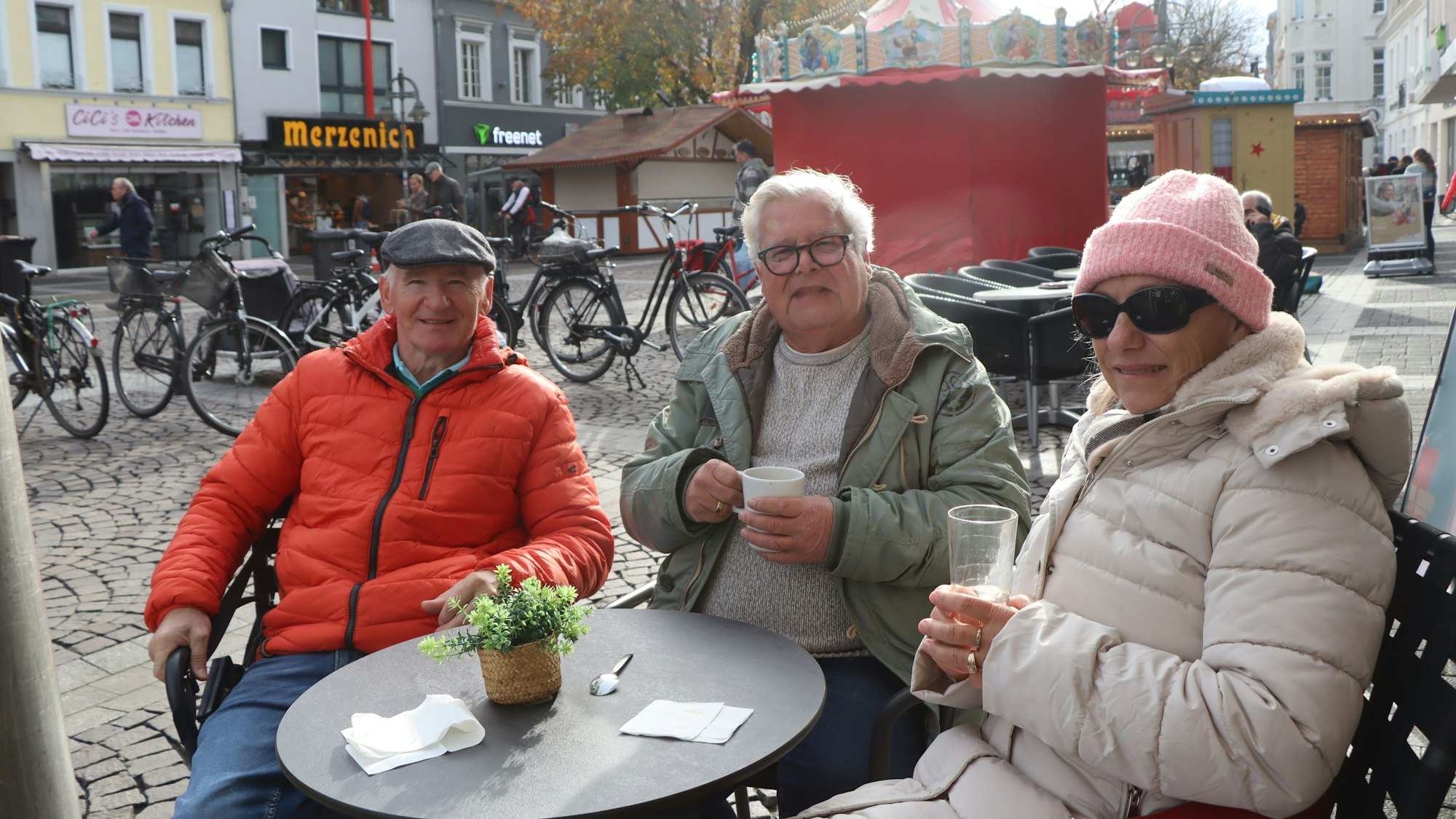 Das Foto zeigt drei Menschen, die in warmer Kleidung draußen Getränke genießen.