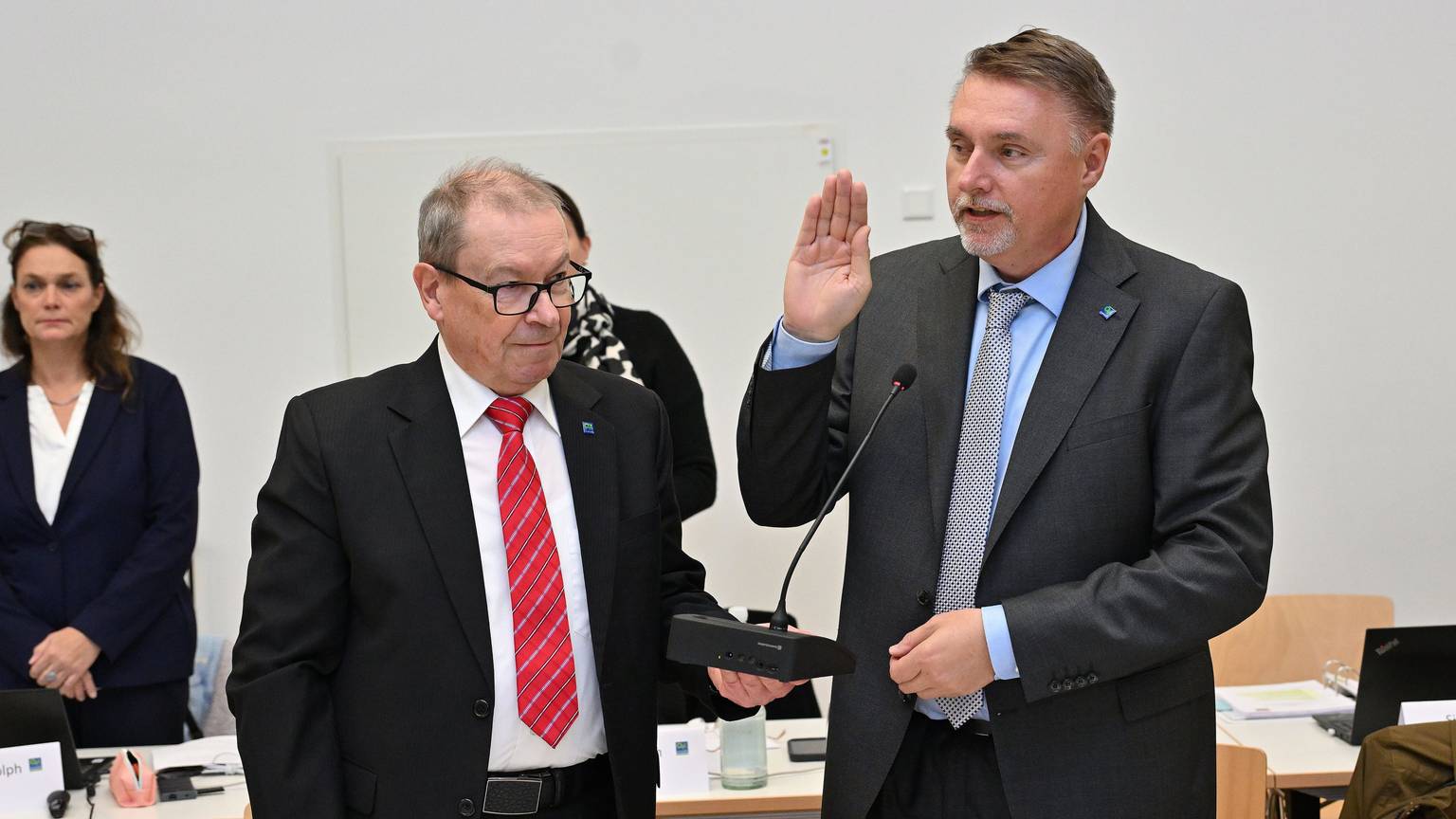 Manfred Meiger von der SPD, steht links neben dem neuen Bürgermeister von Overath, Michael Eyer von der CDU. Eyer hält die Hand flach nach oben gestreckt und spricht den Amtseid nach während Meiger ihm ein Mikrofon hinhält.