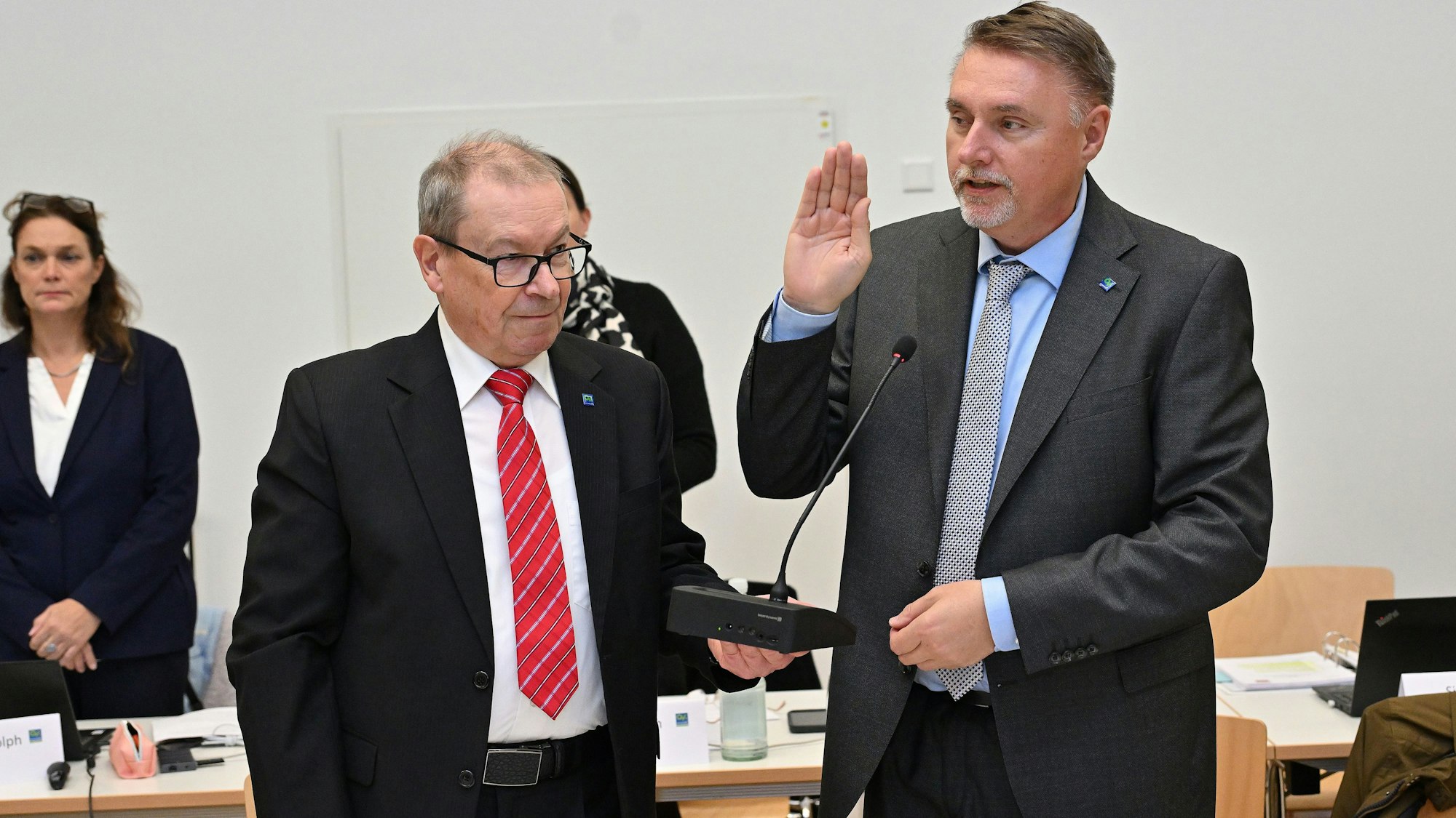 Manfred Meiger von der SPD, steht links neben dem neuen Bürgermeister von Overath, Michael Eyer von der CDU. Eyer hält die Hand flach nach oben gestreckt und spricht den Amtseid nach während Meiger ihm ein Mikrofon hinhält.