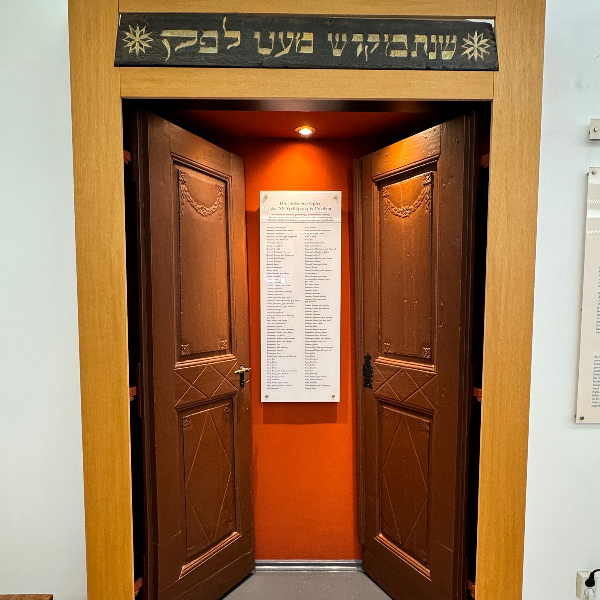 Eine Tür, beide Flügel sind nach innen geöffnet, sie geben den Blick frei auf eine Gedenktafel.