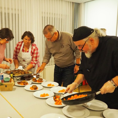 Zwei Männer und zwei Frauen füllen Essen auf Teller.