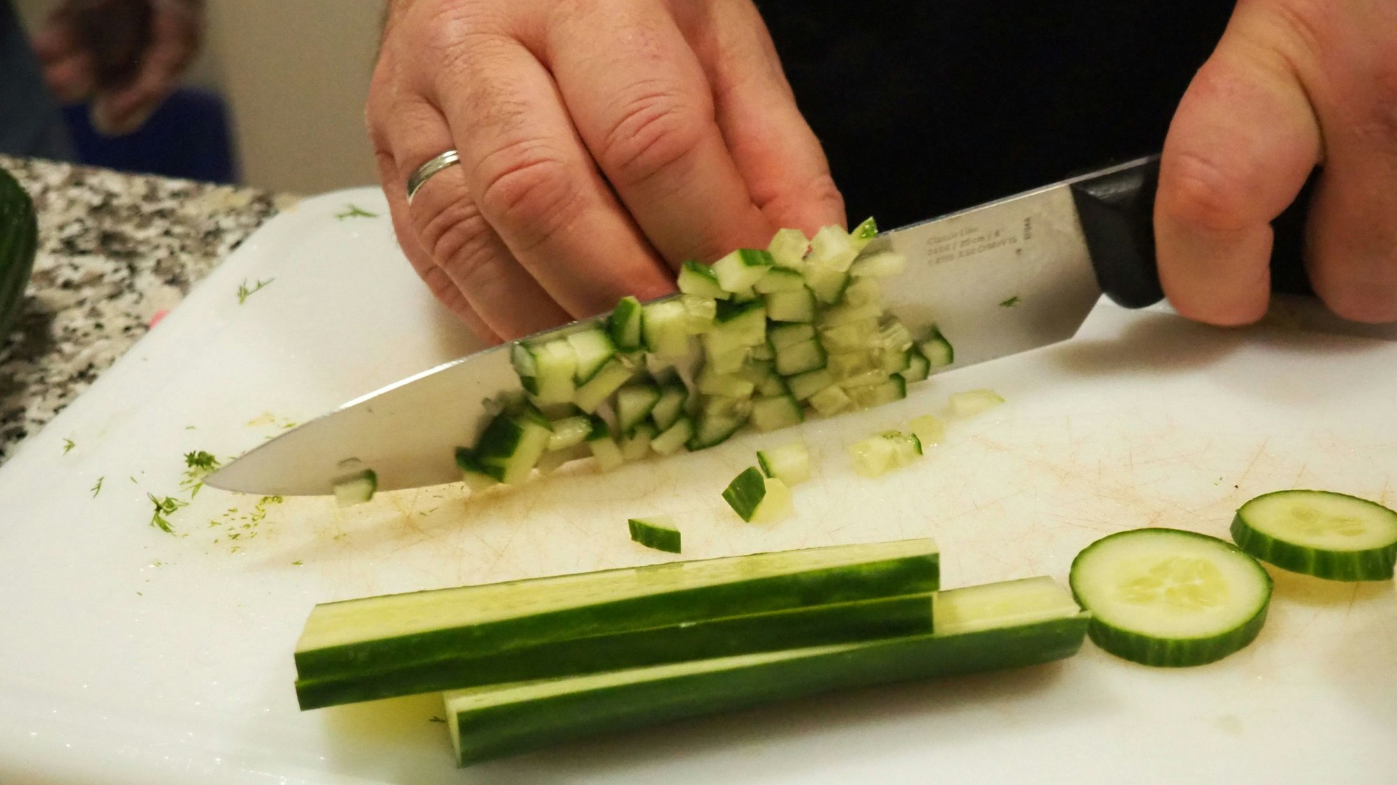 Mit einem großen Messer würfelt jemand eine Gurke. Zu sehen sind nur die Hand und das Messer.