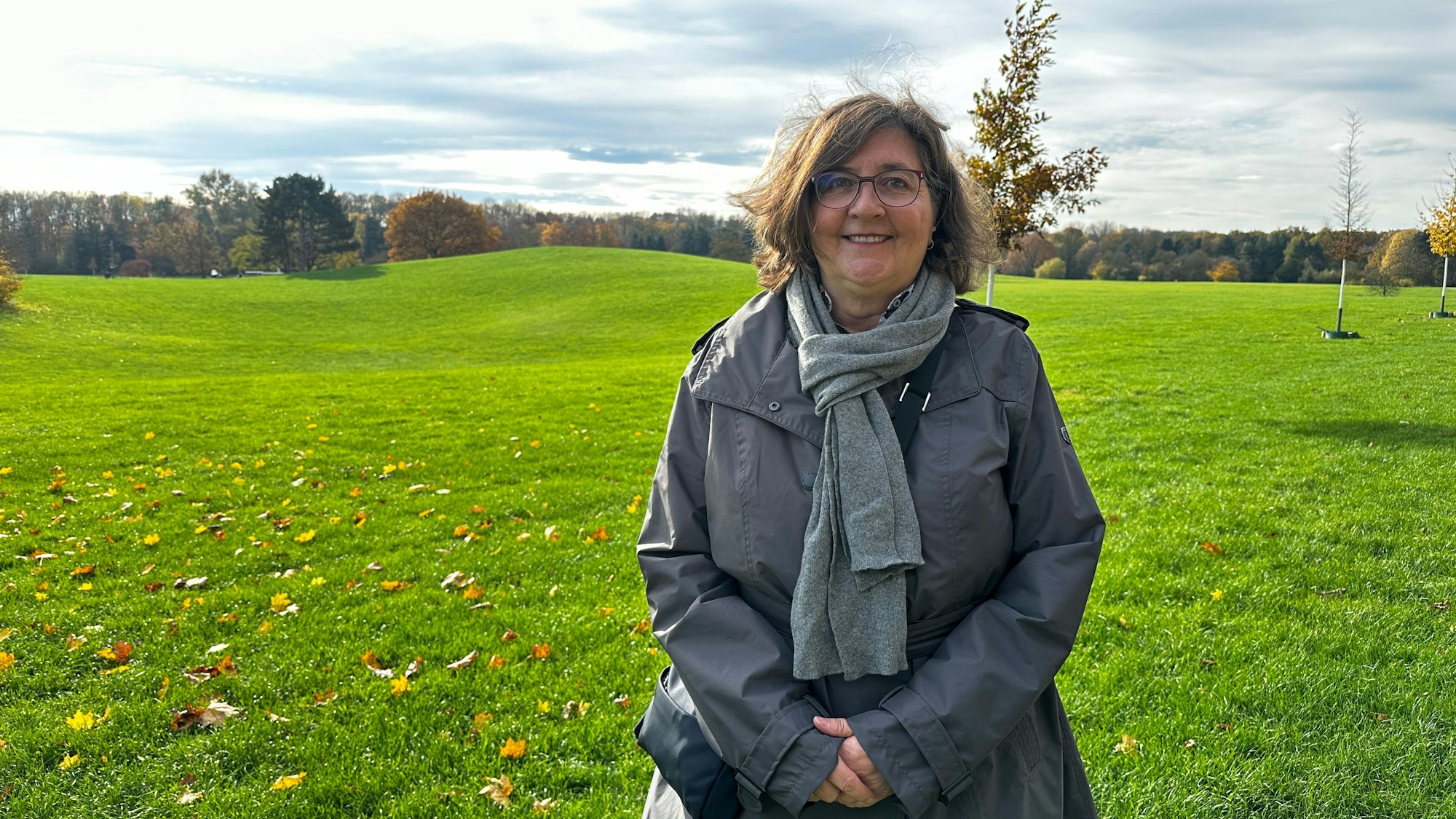Ein Frau, die einen grauen Schal und Anorak trägt, steht auf einer weiten, hügeligen Wiese.