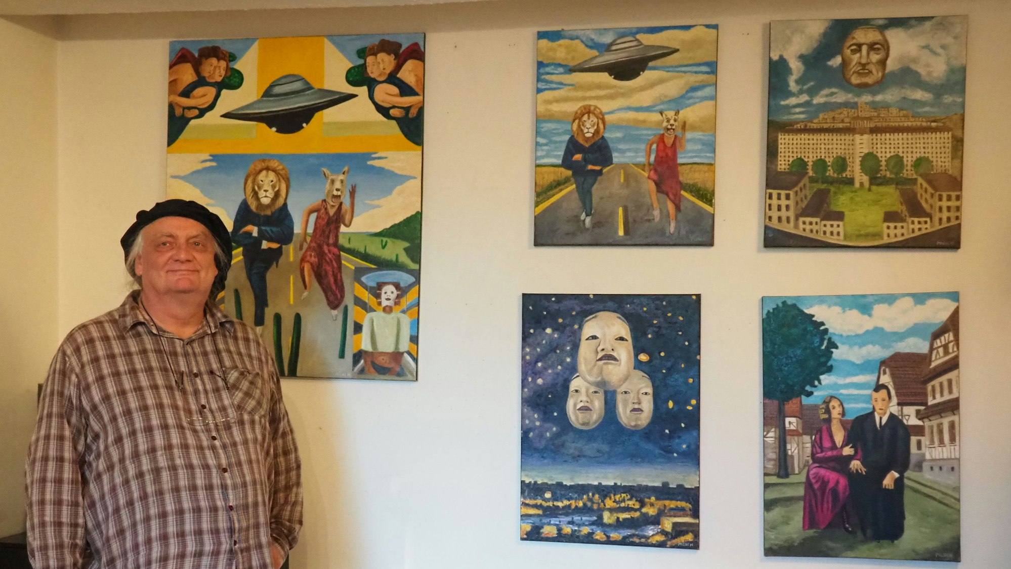 Michael Münch steht vor einer Wand, an der seine Bilder hängen.