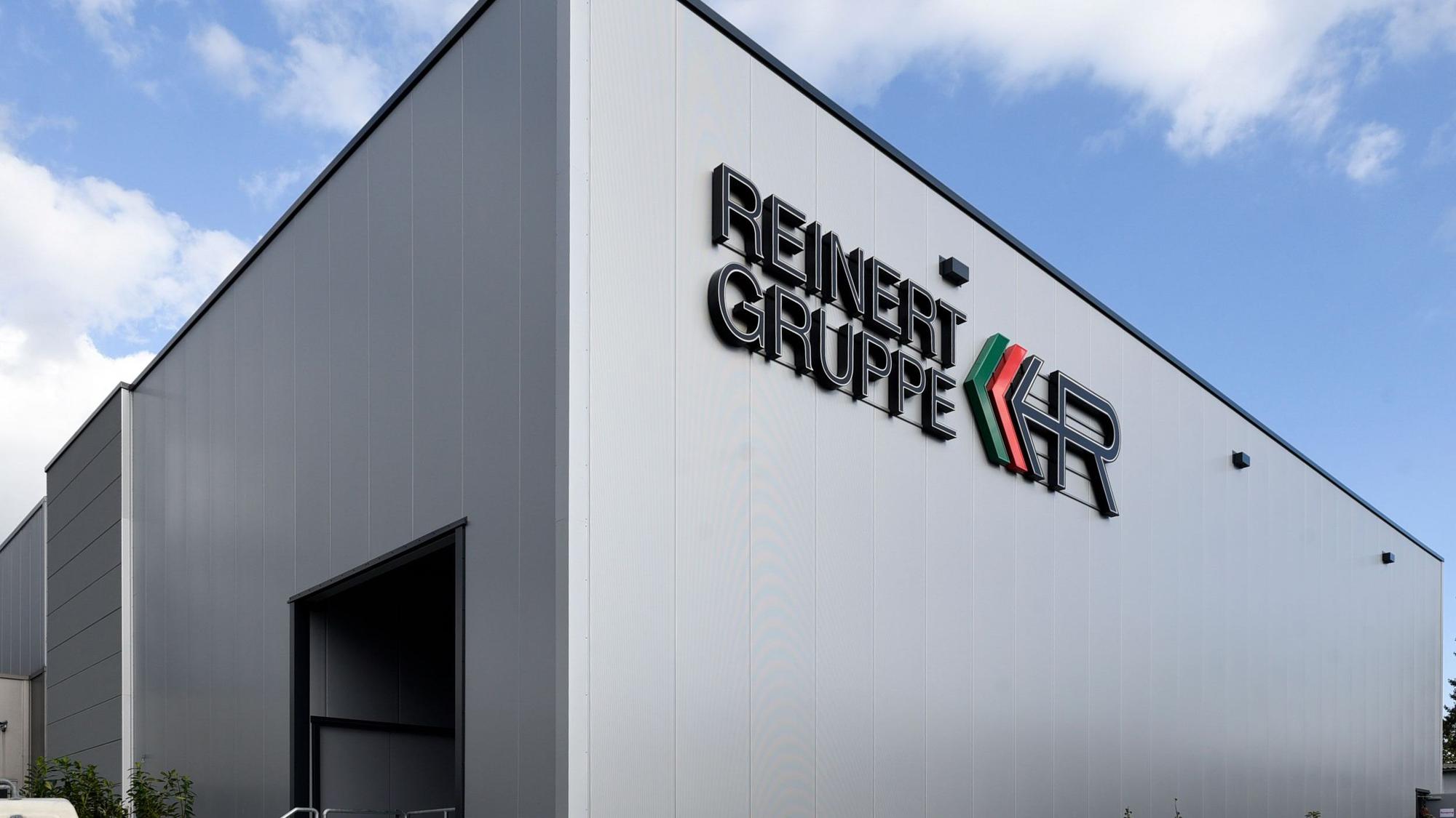 Zu sehen ist eine graue Lagerhalle vor blauem Himmel mit der Aufschrift „Reinert Gruppe“.