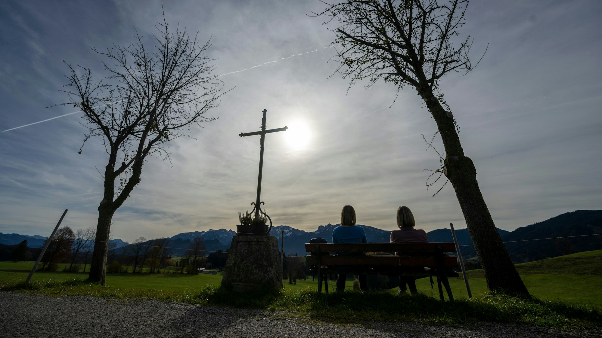 wei Frauen genießen auf eine Bank neben einem Wegkreuz die Herbstsonne.