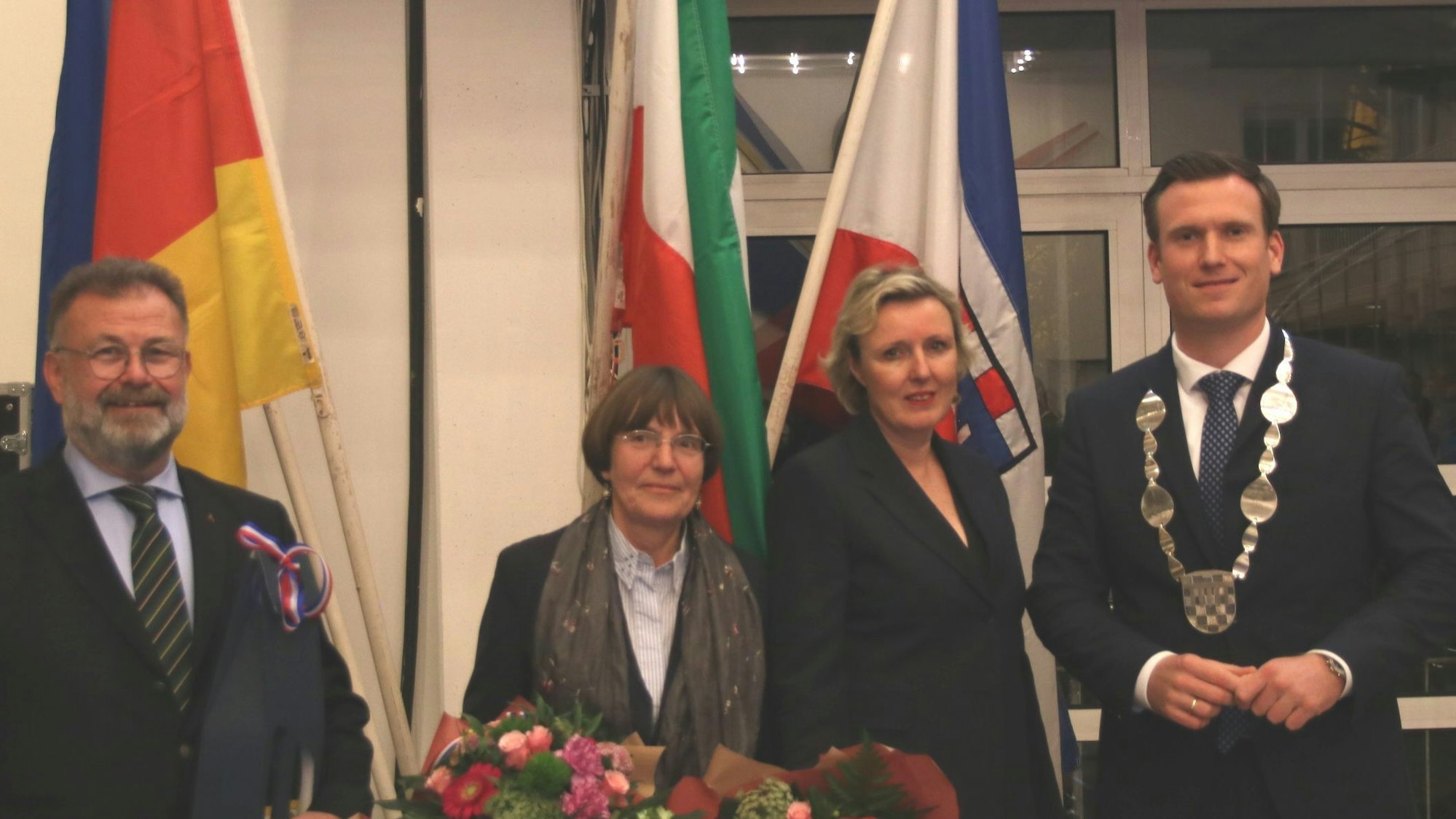 Zwei Männer und zwei Frauen, im Hintergrund verschiedene Flaggen.