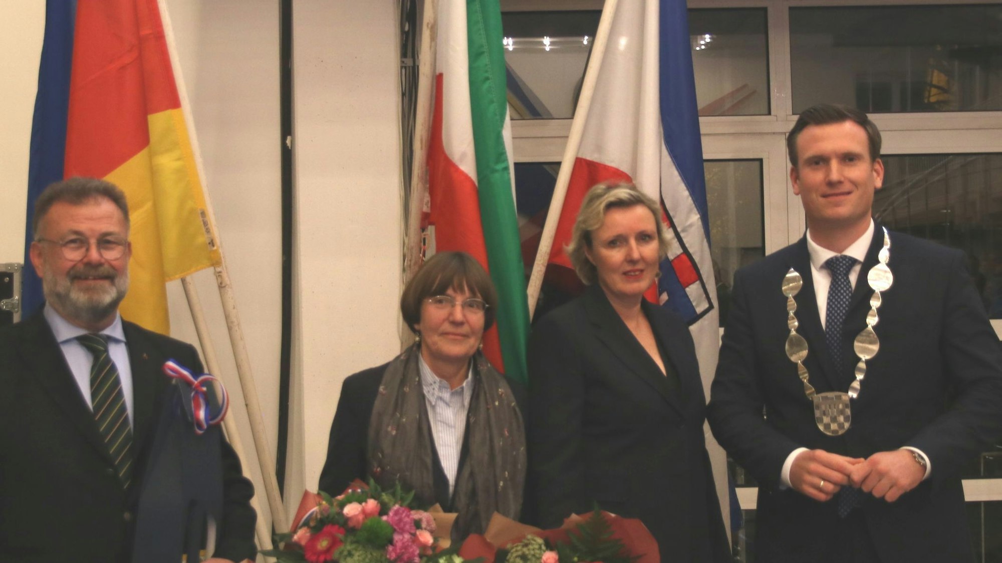 Zwei Männer und zwei Frauen, im Hintergrund verschiedene Flaggen.