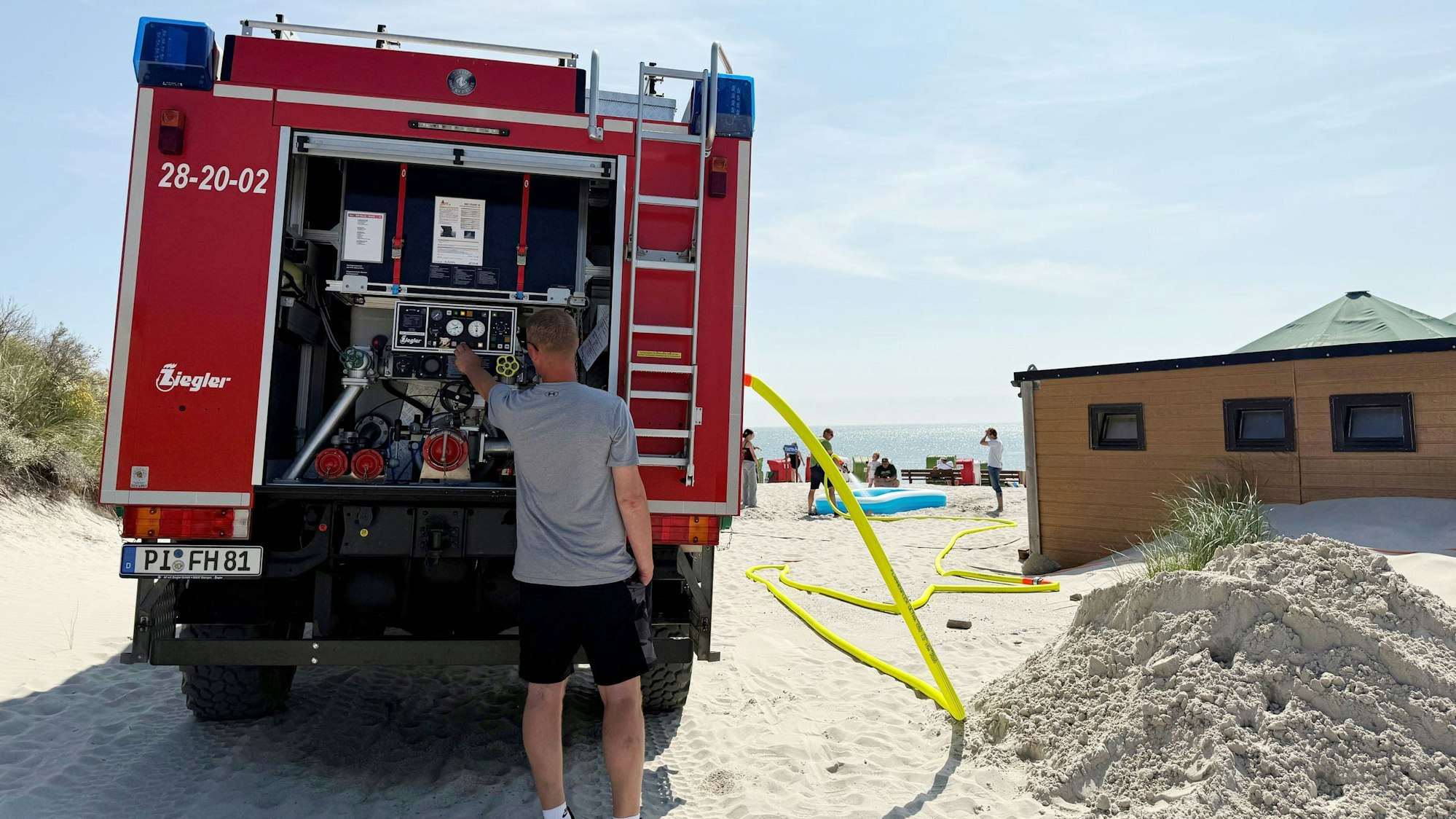 Ein Mann am Feuerwehrauto, ein Schlauch führt zum Strand.