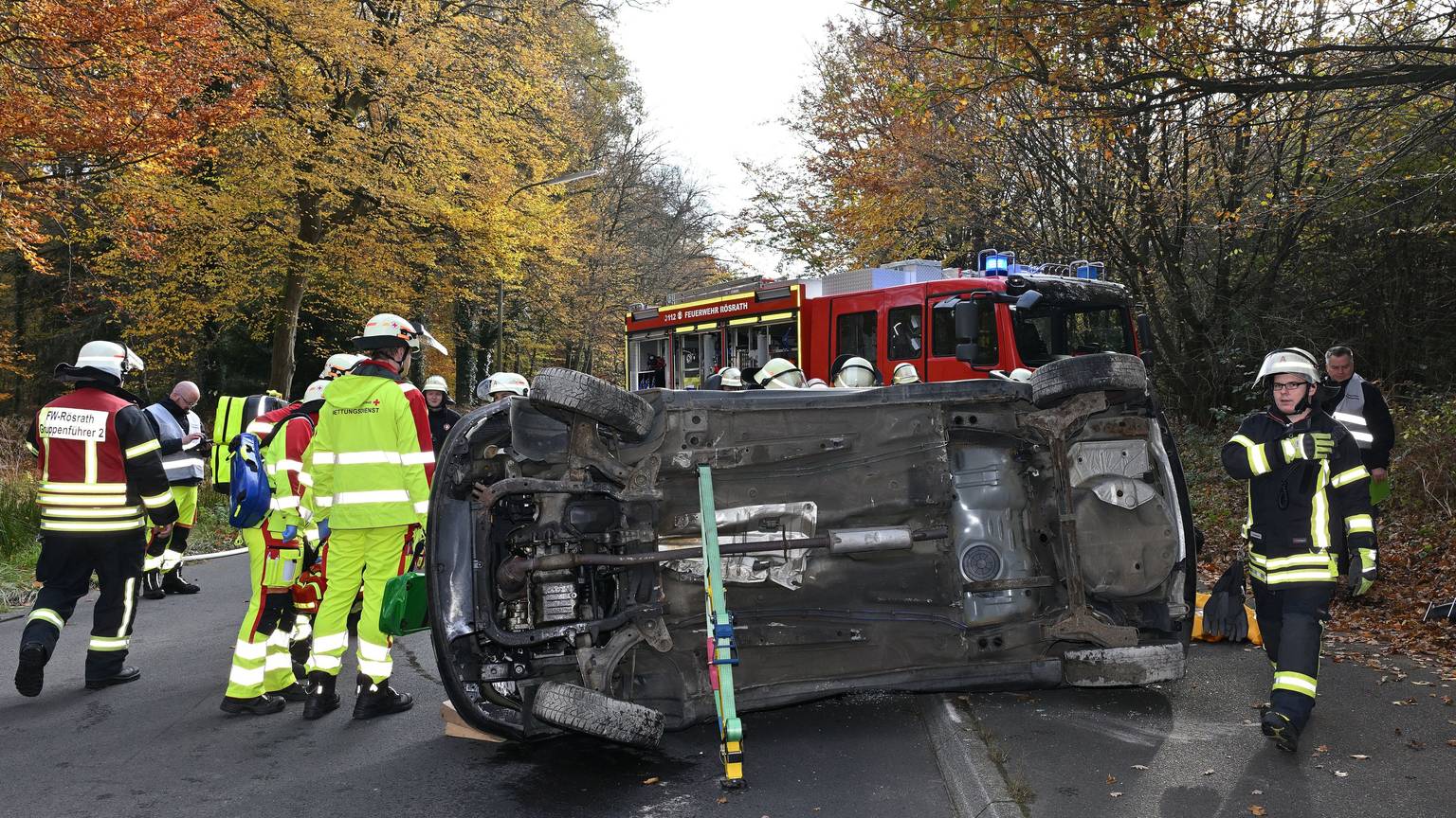 Ein Auto liegt auf der Seite auf der Straße, darum herum Feuerwehrleute.