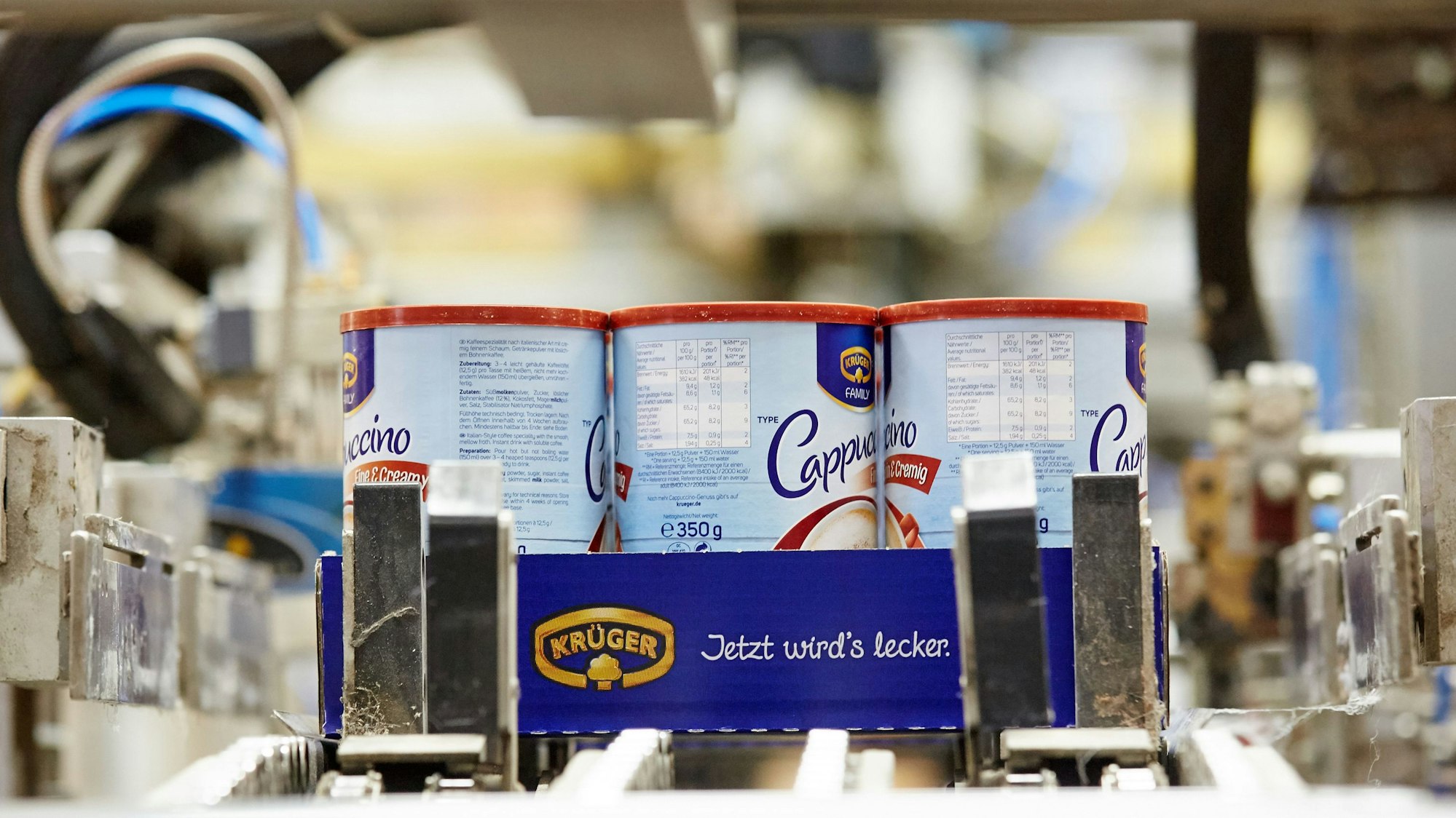 Drei Dosen mit Krüger-Cappuccino auf einem Produktionsband.