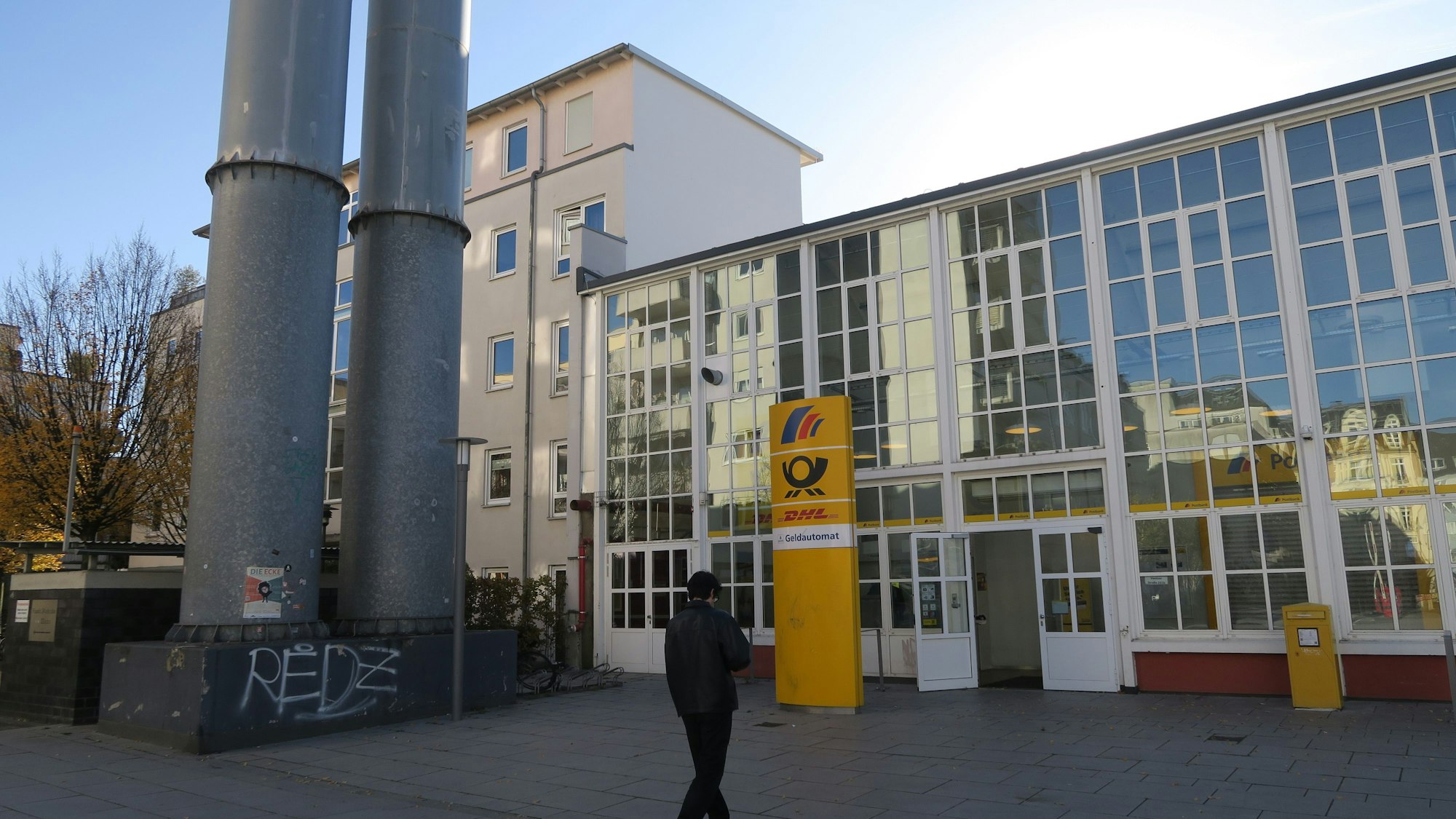 Ein Mann geht auf den Eingang einer Postbank-Filiale zu, die eine große Fensterfront hat.