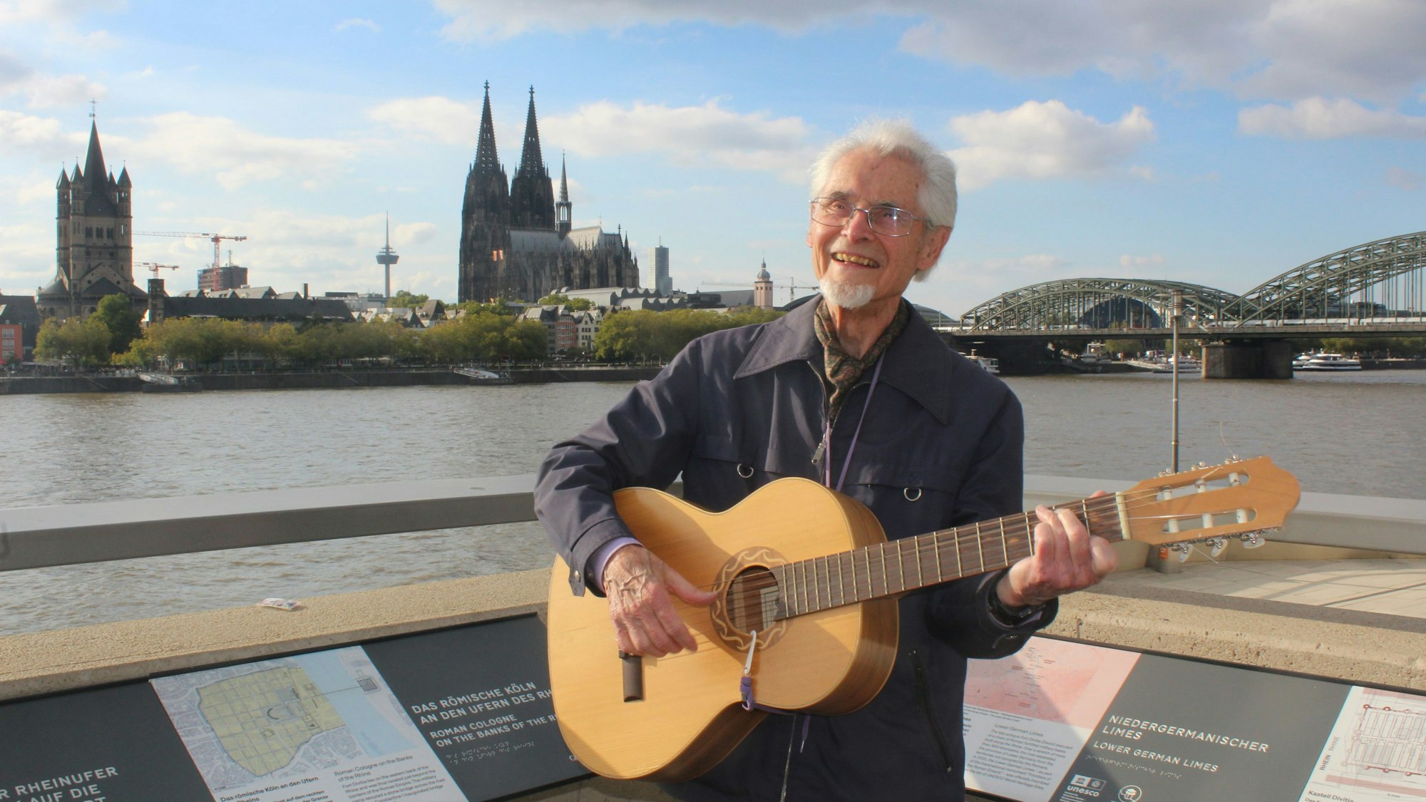 Willi Potthoff steht mit seiner Gitarre auf der rechtsrheinischen Seite mit Blick auf den Dom.