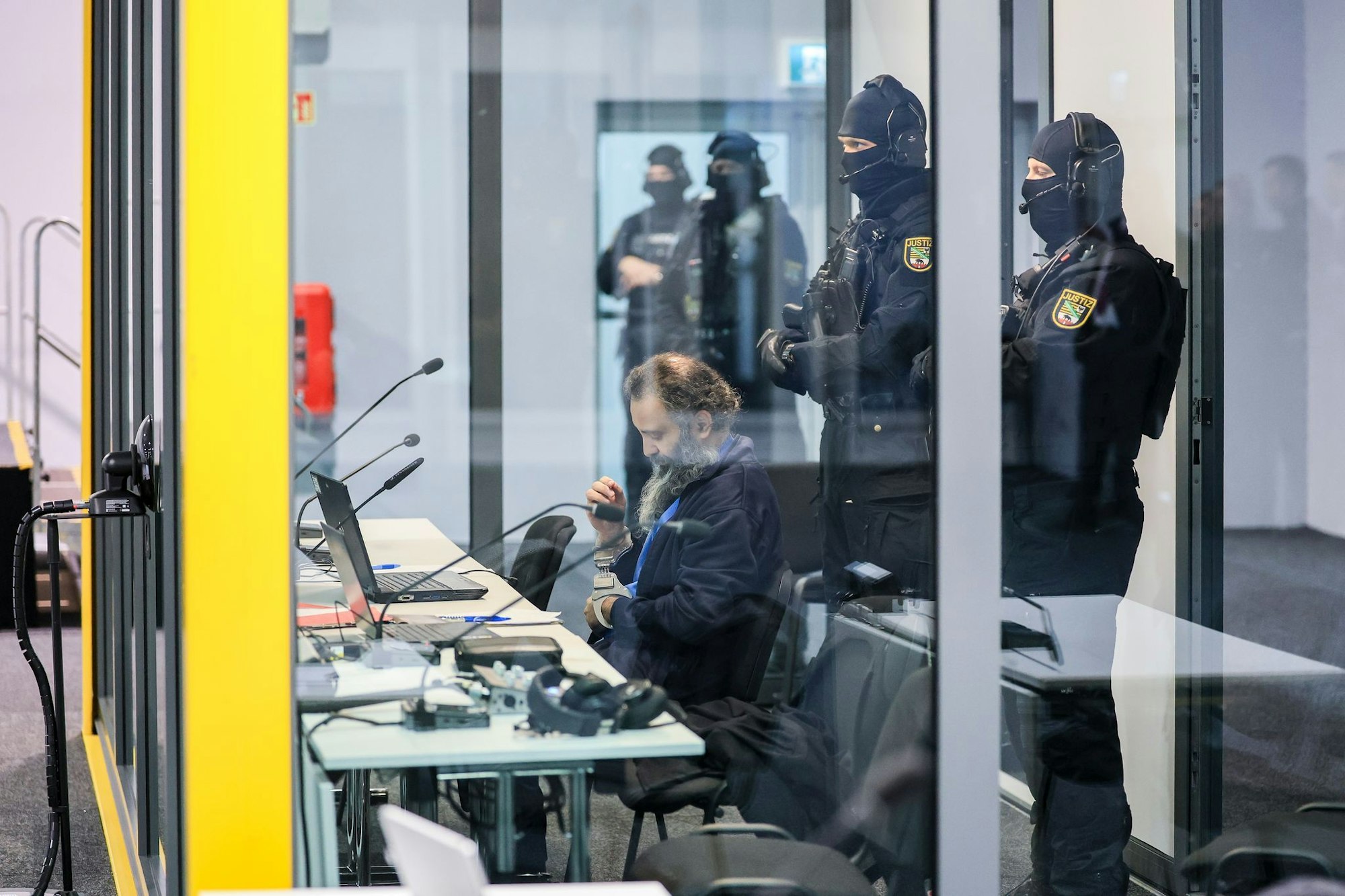 Der Angeklagte Taleb al-Abdulmohsen sitzt mit Handfesseln in dem kugelsicheren Glaskasten im temporären Gerichtsgebäude des Landgerichtes Magdeburg.