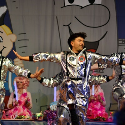 Drei Männer in silbernen Weltraum-Kostümen tanzen auf der Bühne.