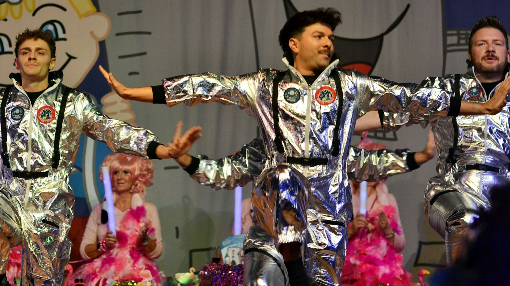 Drei Männer in silbernen Weltraum-Kostümen tanzen auf der Bühne.