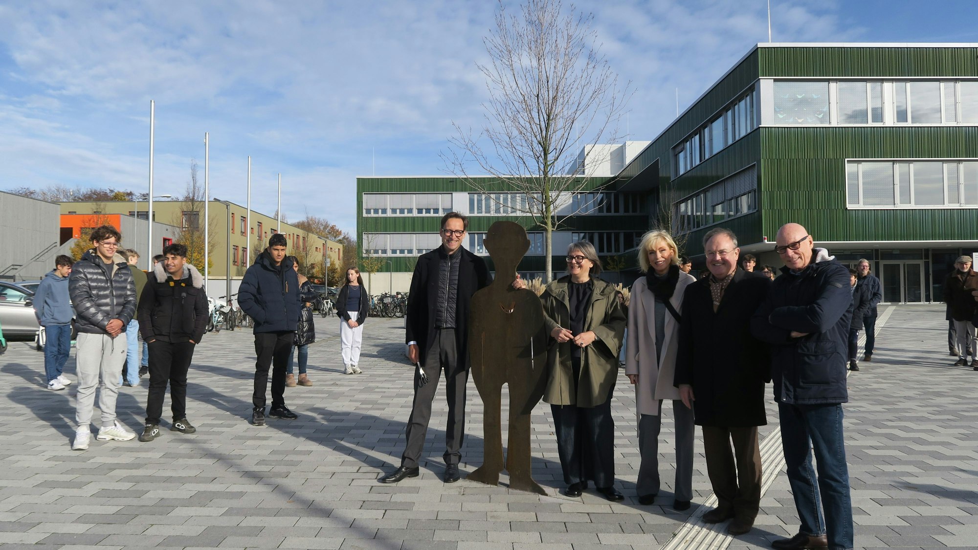 Erwachsene und Schüler stellen umrahmen eine Figur aus Cortenstahl, die auf dem Schulhof aufgestellt wurden.