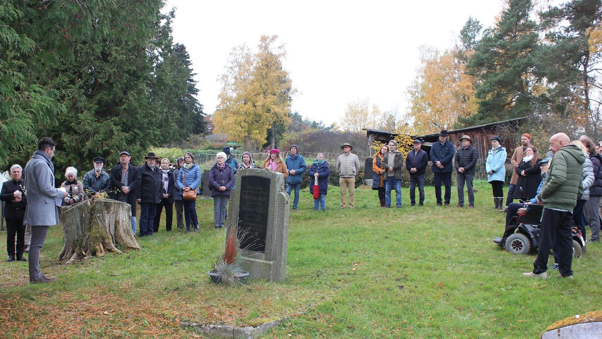 Menschen stehen in einem Halbkreis auf dem jüdischen Friedhof.
