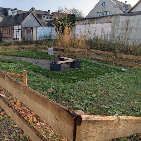 Das Foto zeigt die kleine, etwas verwildert wirkende Grünanlage hinter einem Bretterzaun.