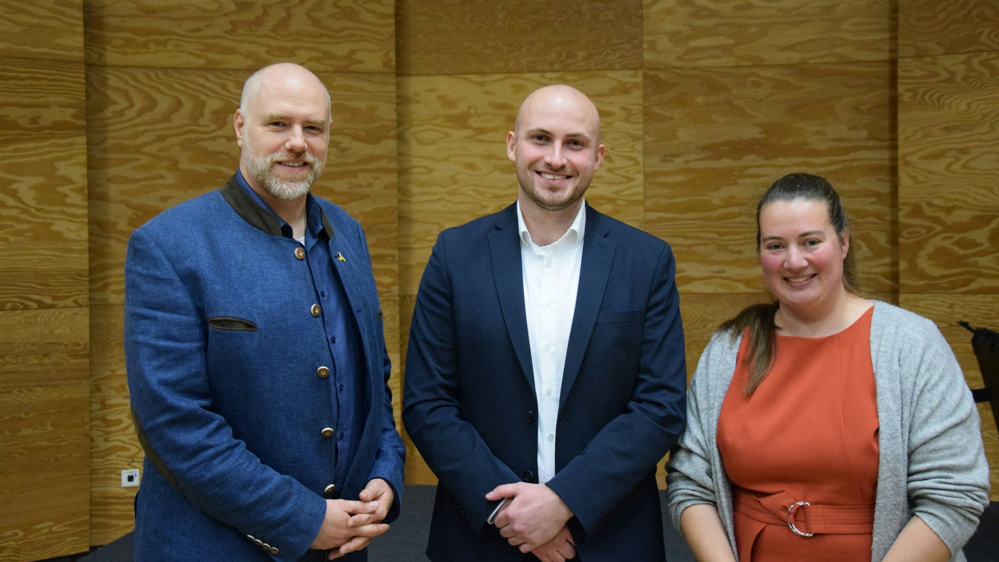 Zwei Männer und eine Frau stehen nebeneinander und lachen in die Kamera.