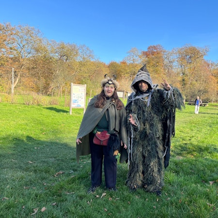 Zwei verkleidete Frauen stehen in Waldgeist-Kostümen auf einer Wiese.