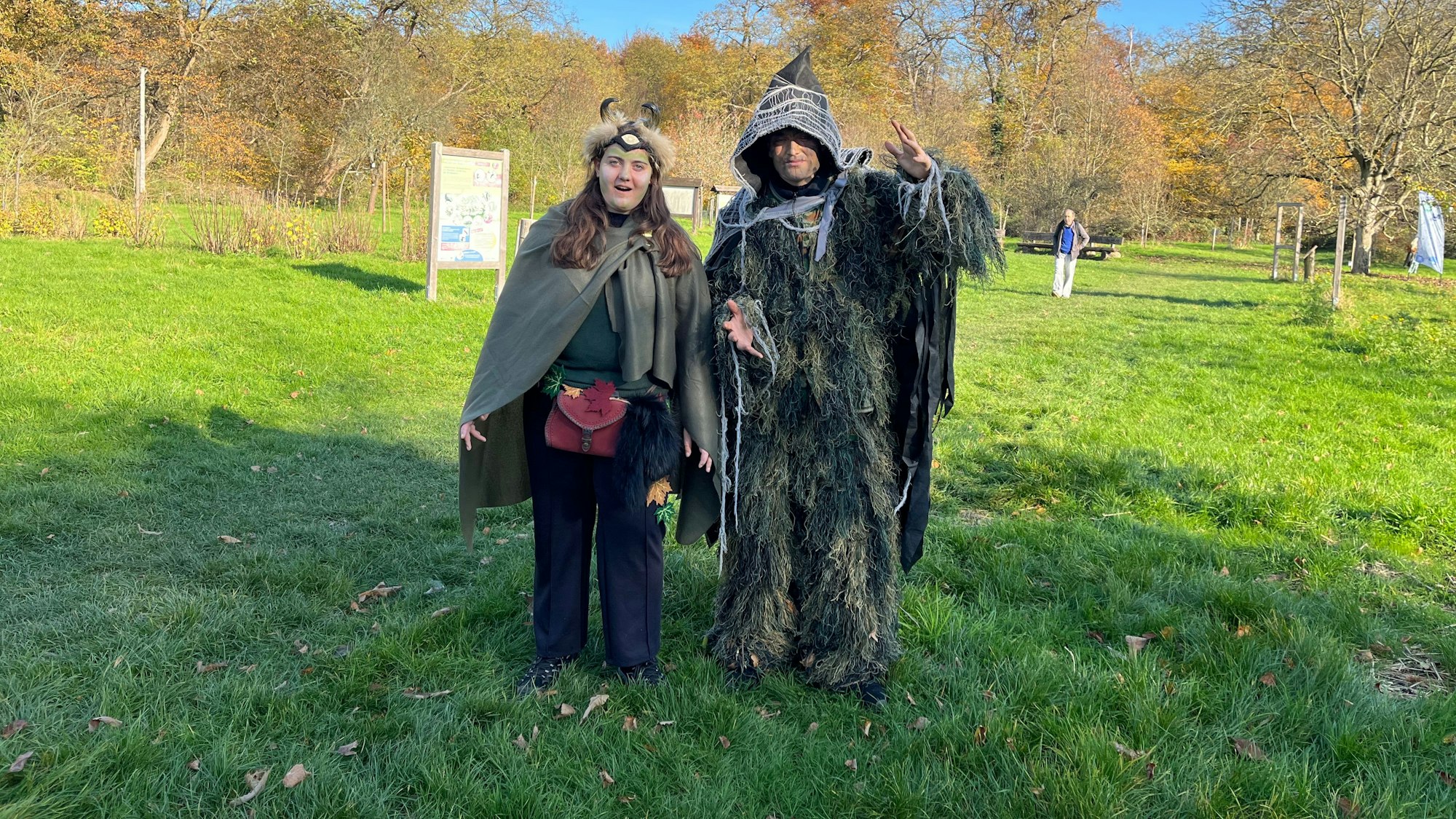 Zwei verkleidete Frauen stehen in Waldgeist-Kostümen auf einer Wiese.
