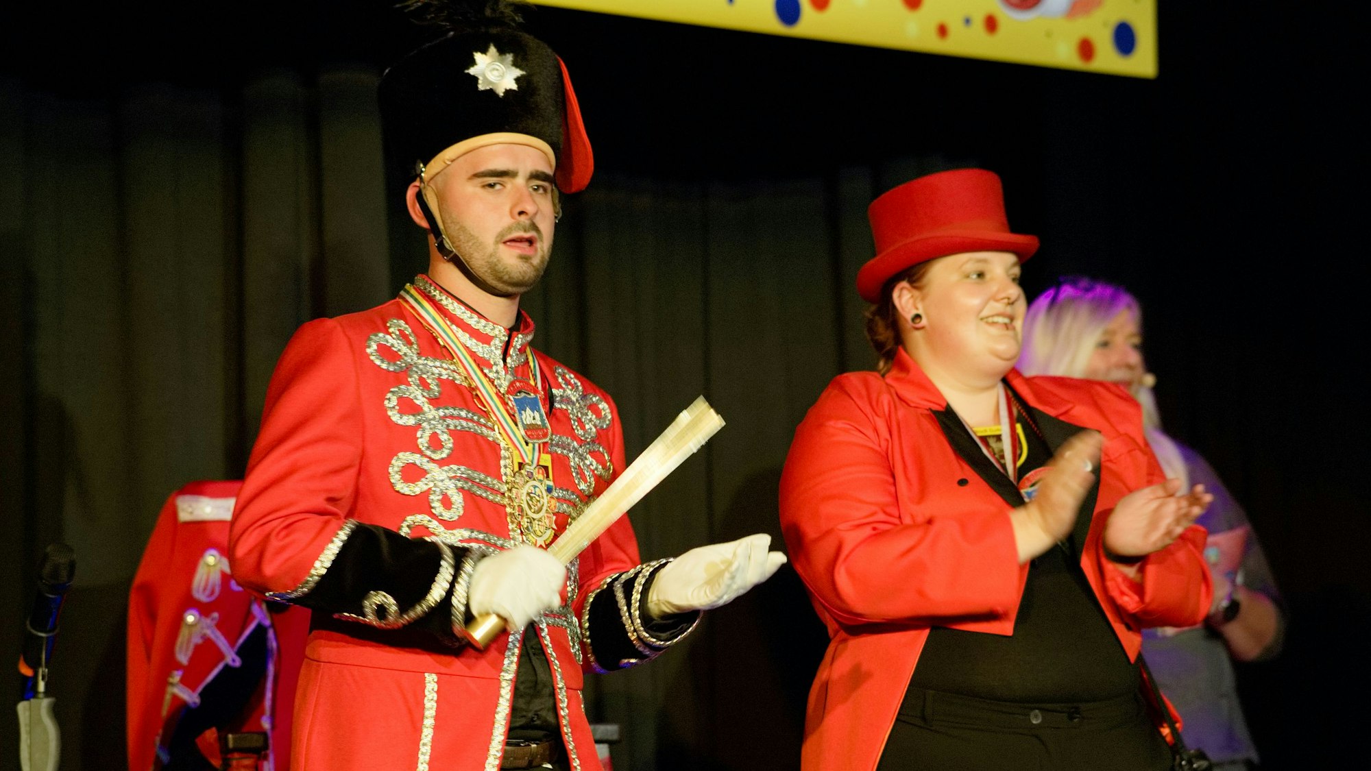 Robert Herter trägt eine rote Uniform, neben ihm steht eine ebenfalls rot gekleidete Frau.