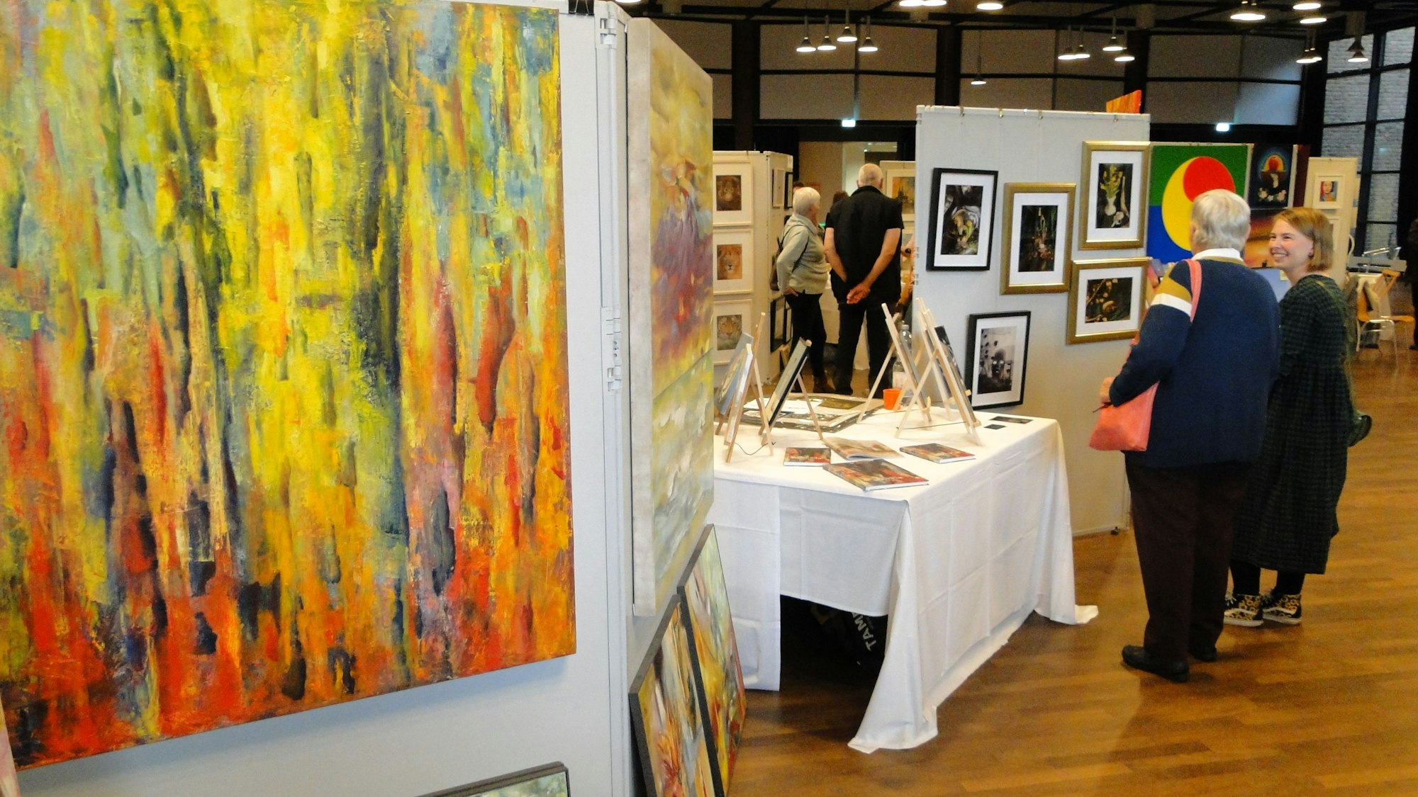 In einem großen Saal sind Gemälde an Stellwänden aufgehängt, Menschen schlendern durch den Raum.