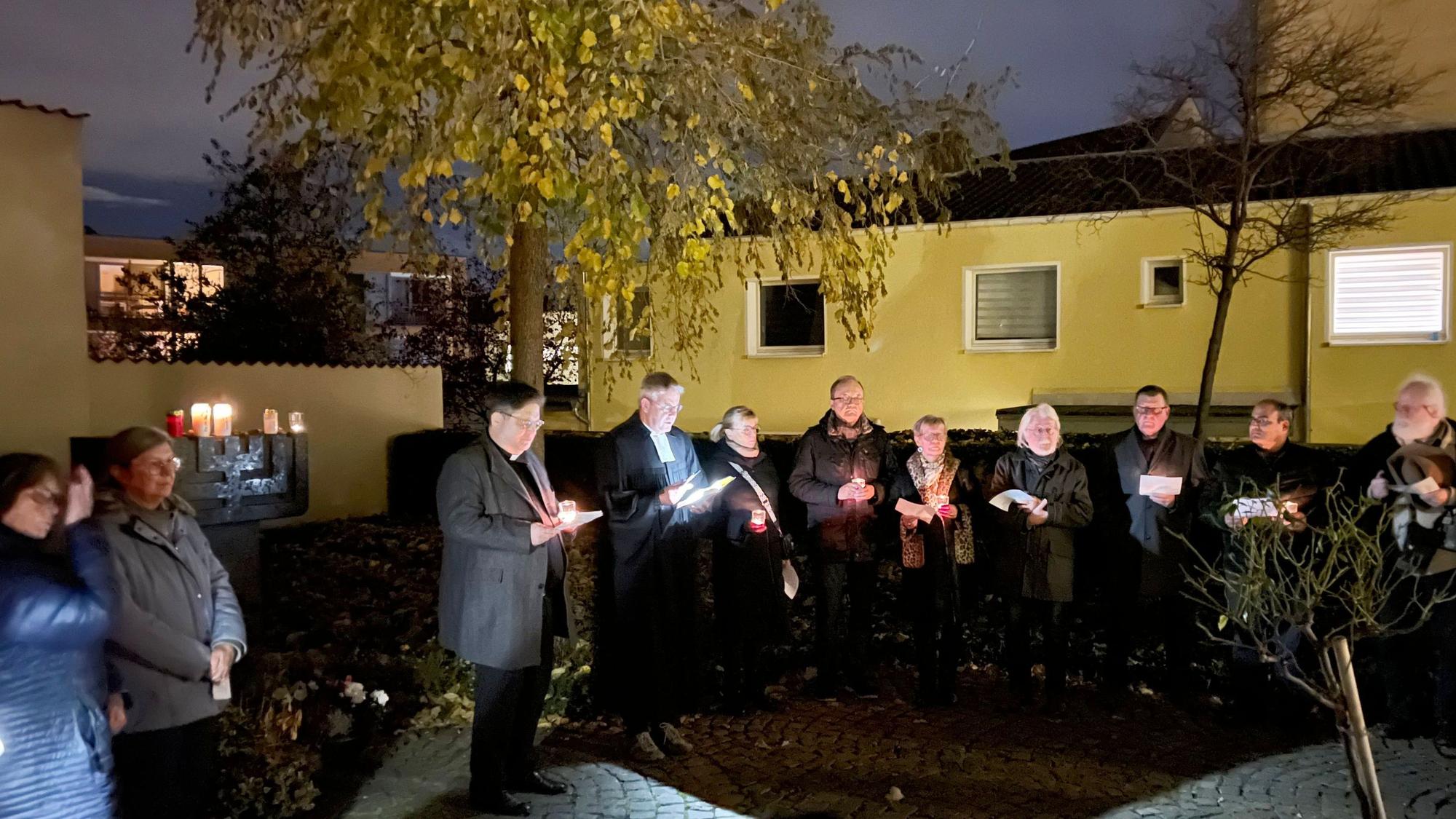 Frauen und Männer stehen, mit Kerzen in der Hand, singend in einer Reihe.