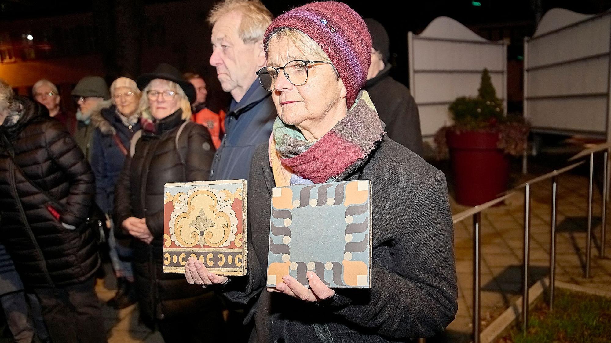 Eine Frau hält zwei alte, bunte Bodenfliesen in den Händen, die aus dem abgerissenen Haus Risa gerettet wurden.