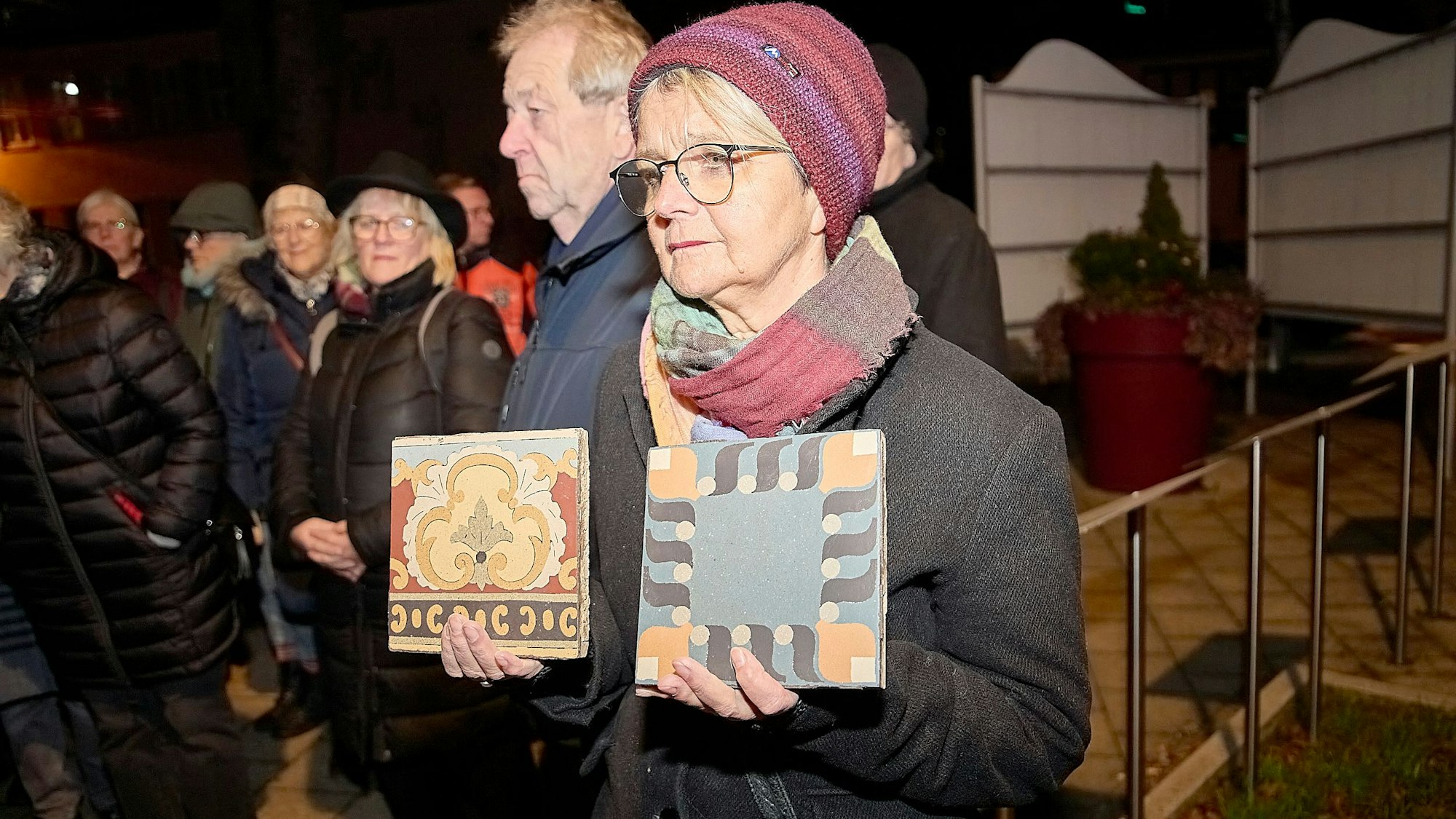 Eine Frau hält zwei alte, bunte Bodenfliesen in den Händen, die aus dem abgerissenen Haus Risa gerettet wurden.