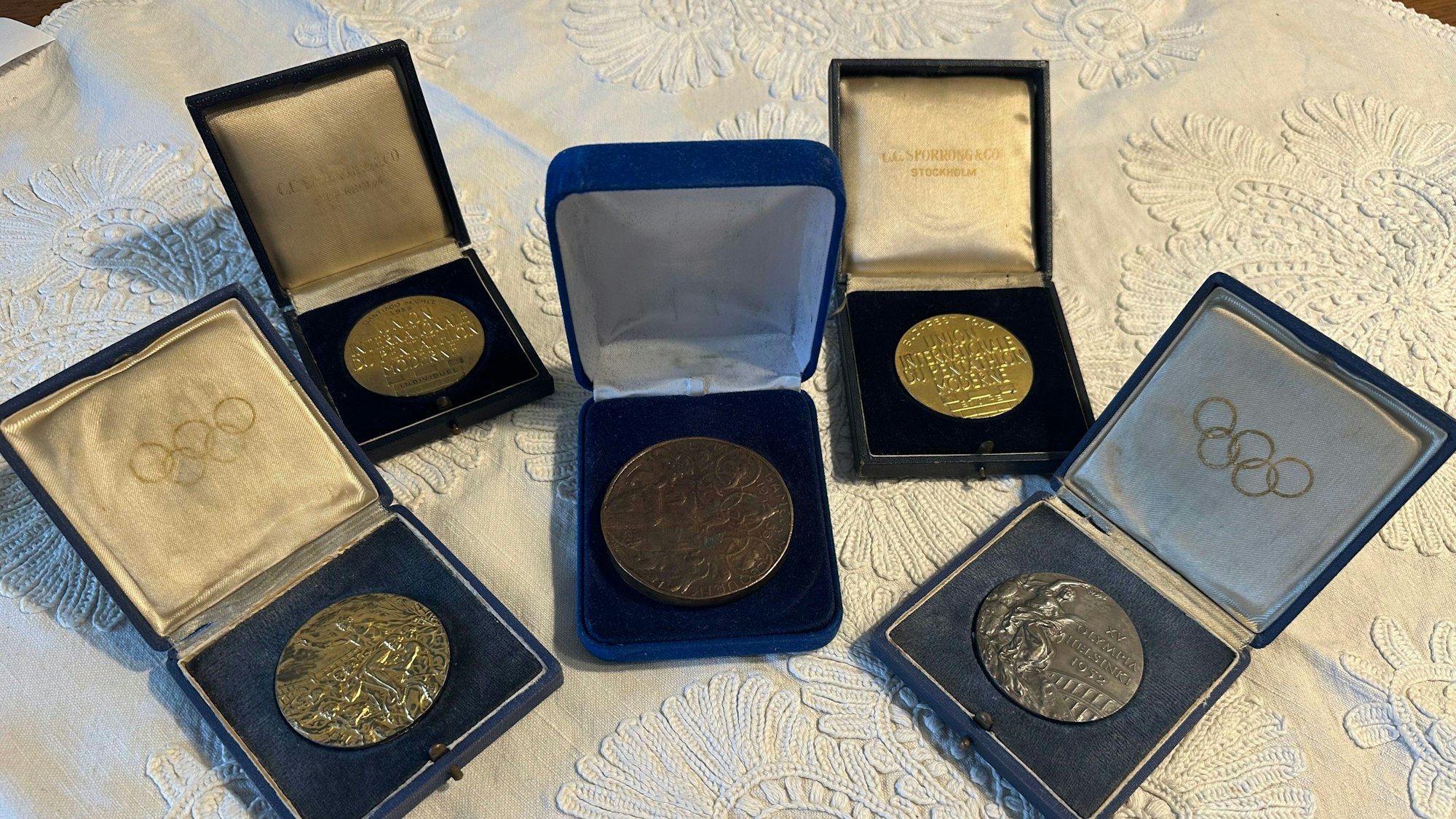 Links die Goldmedaille, rechts die Silbermedaille von Olympia in Helsinki, in der Mitte die Teilnahmemedaille aus Melbourne, hinten die beiden Medaillen als Weltmeister im Modernen Fünfkampf.