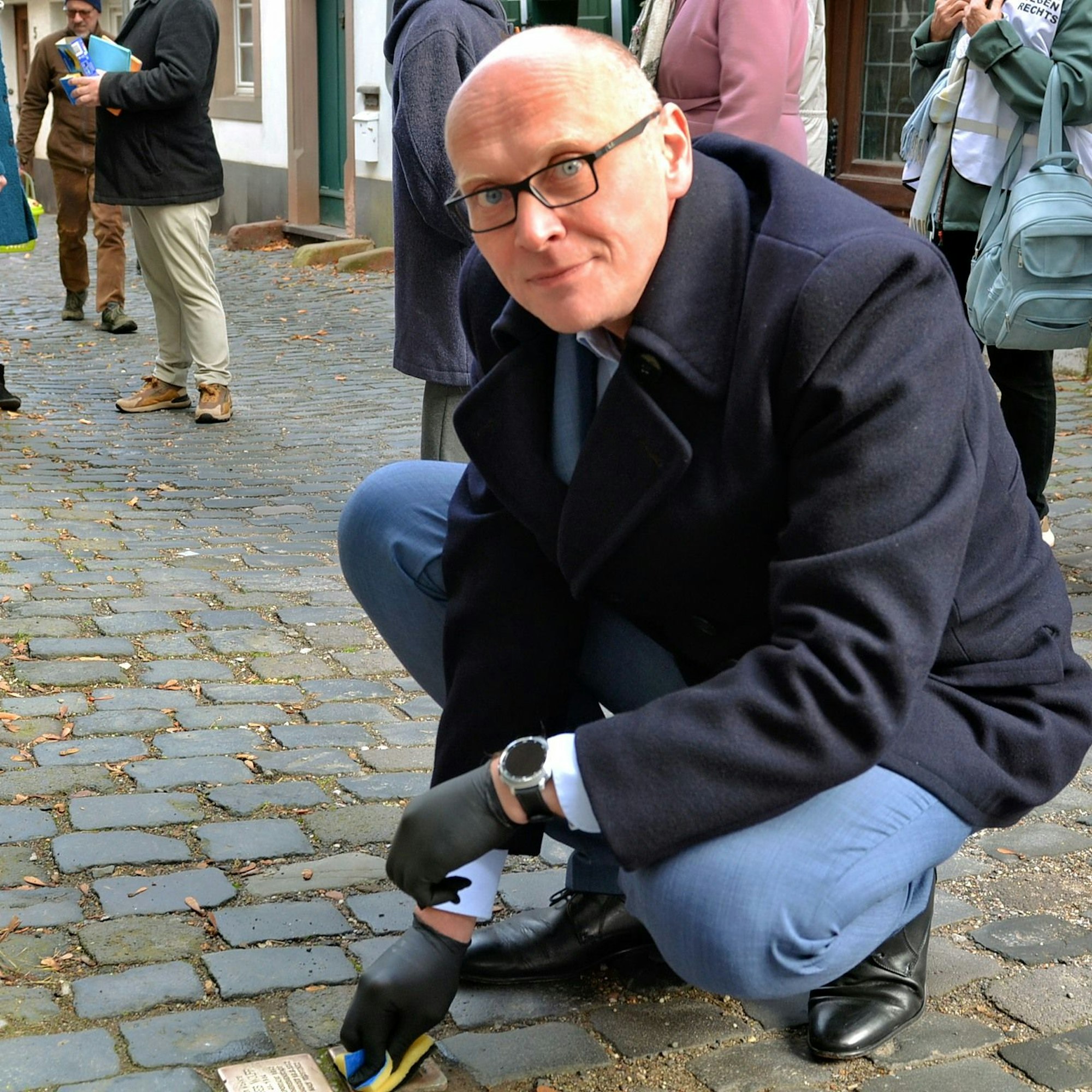 Hockend reinigt Bürgermeister Sebastian Glatzel die Stolpersteine im Pflaster.