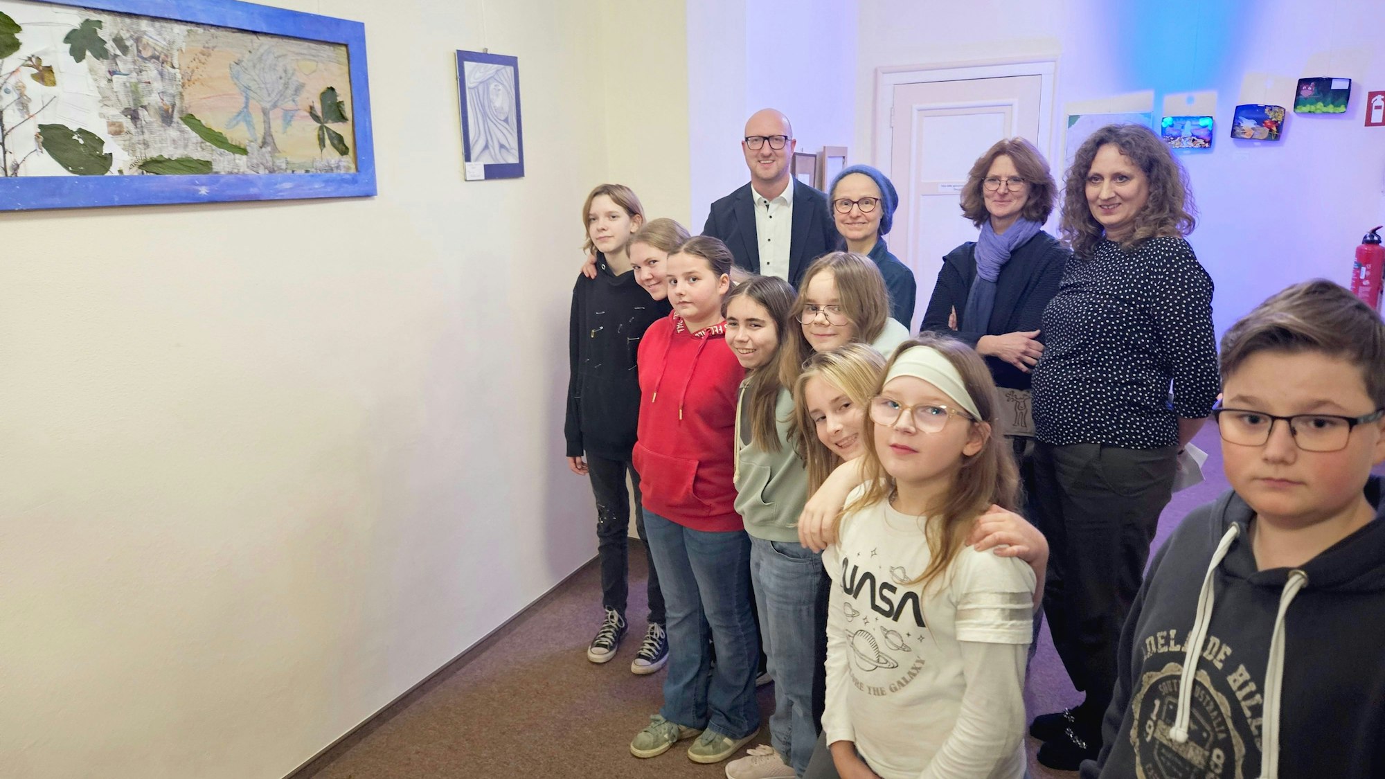 Die jungen Künstler stehen nebeneinander vor den Bildern. Die Erwachsenen stehen dahinter.
