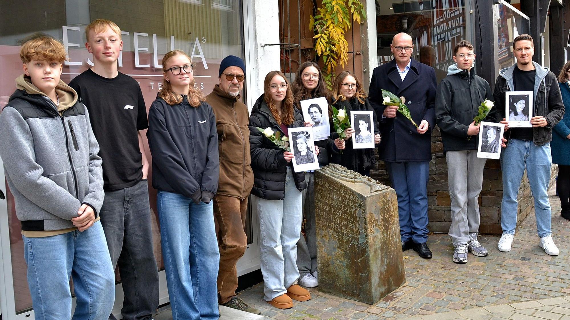 Am Gedenkstein der einstigen Synagoge in Bad Münstereifel stehen einige Menschen. Manche halten Schwarz-Weiß-Fotos oder weiße Rosen in den Händen.