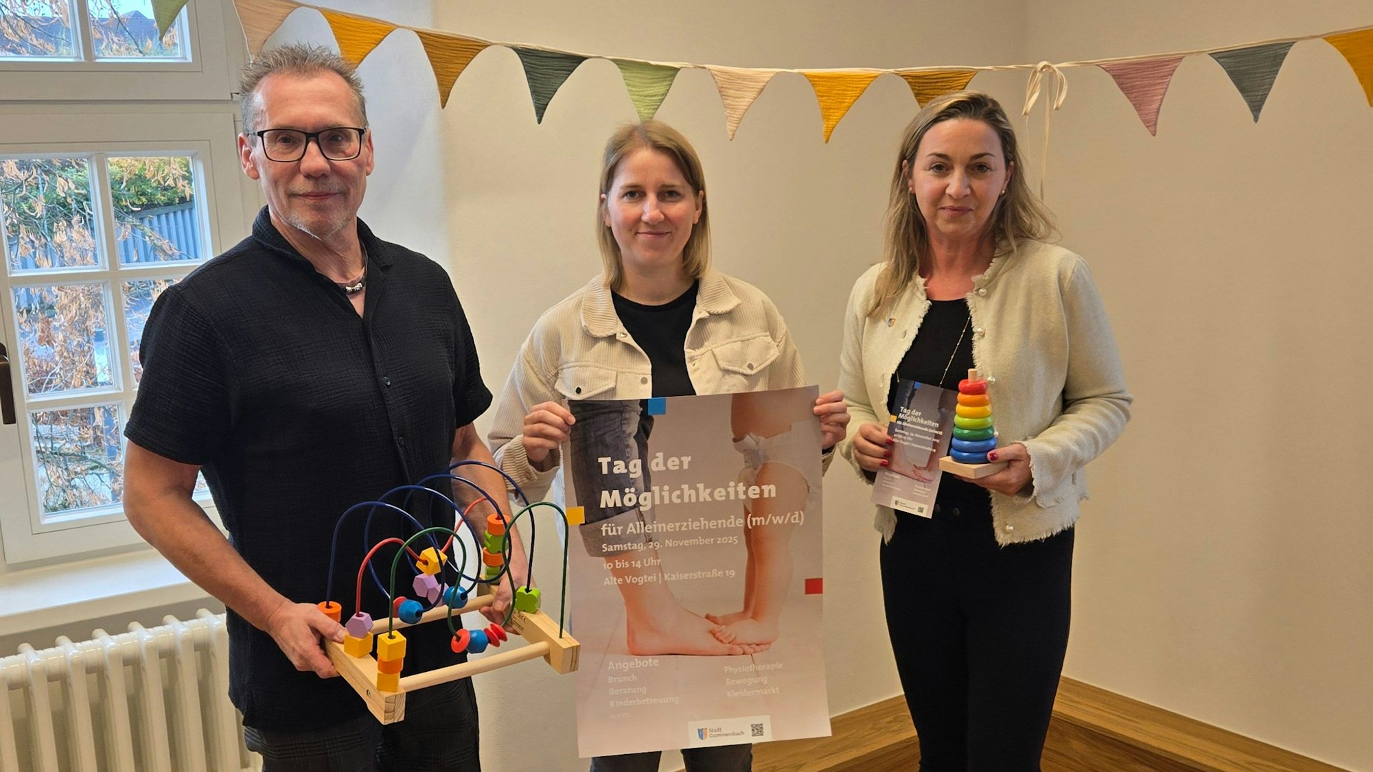 Drei Personen, eine hält ein Plakat, die anderen Spielzeug.