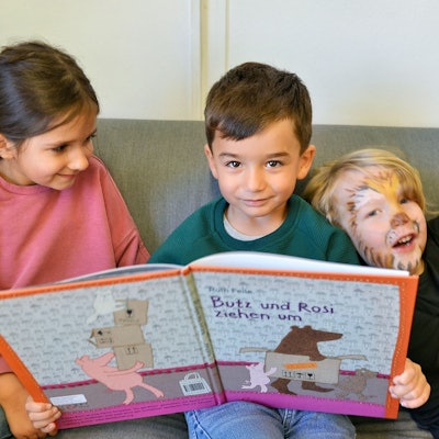 Drei Kinder schauen sich in der Kita „Wirbelwind“ ein Bilderbuch an.