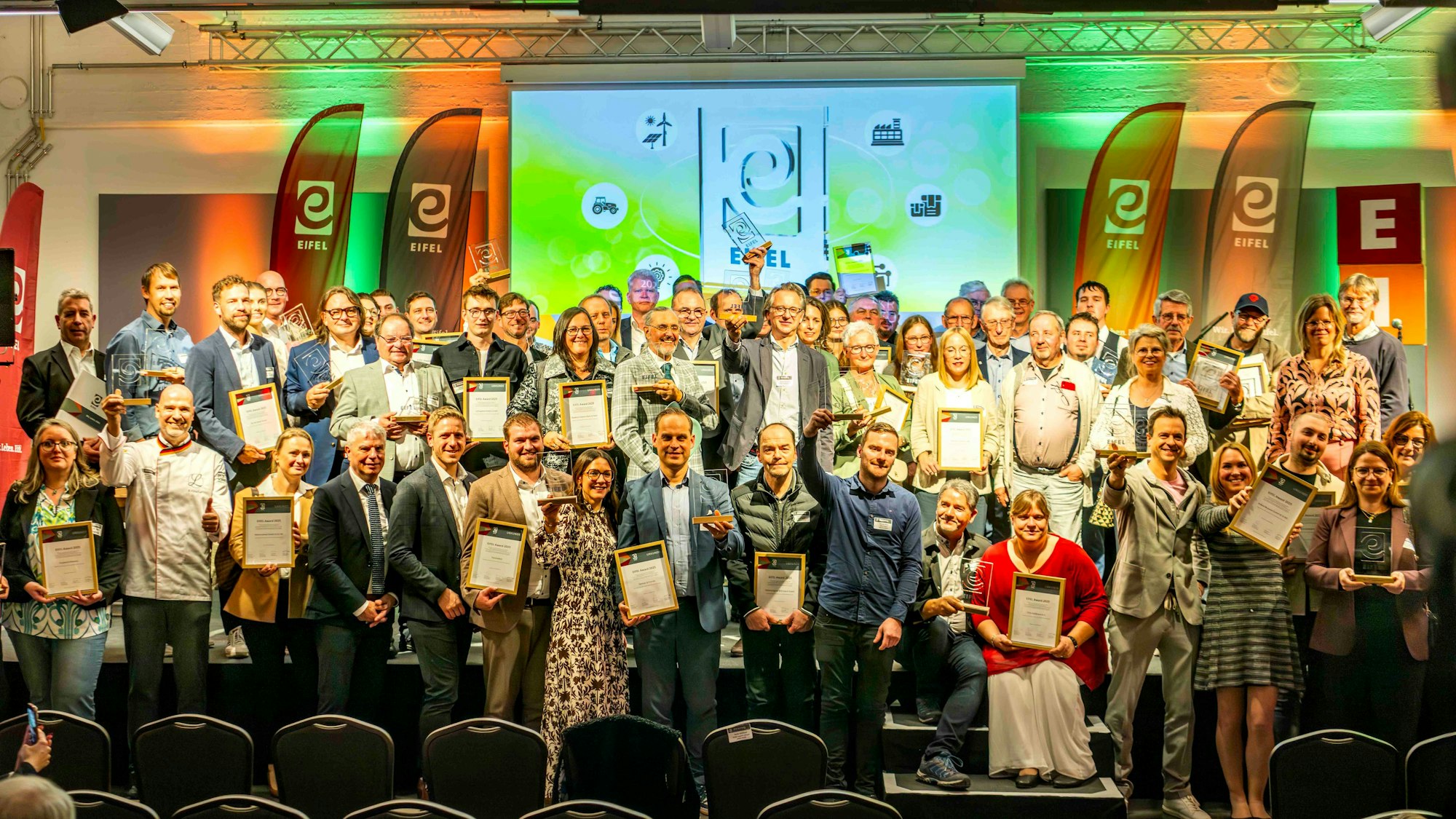 Zahlreiche Menschen stehen auf der Bühne in der Feuerhalle der Alten Tuchfabrik in Euskirchen. Die meisten halten gerahmte Urkunden in den Händen.