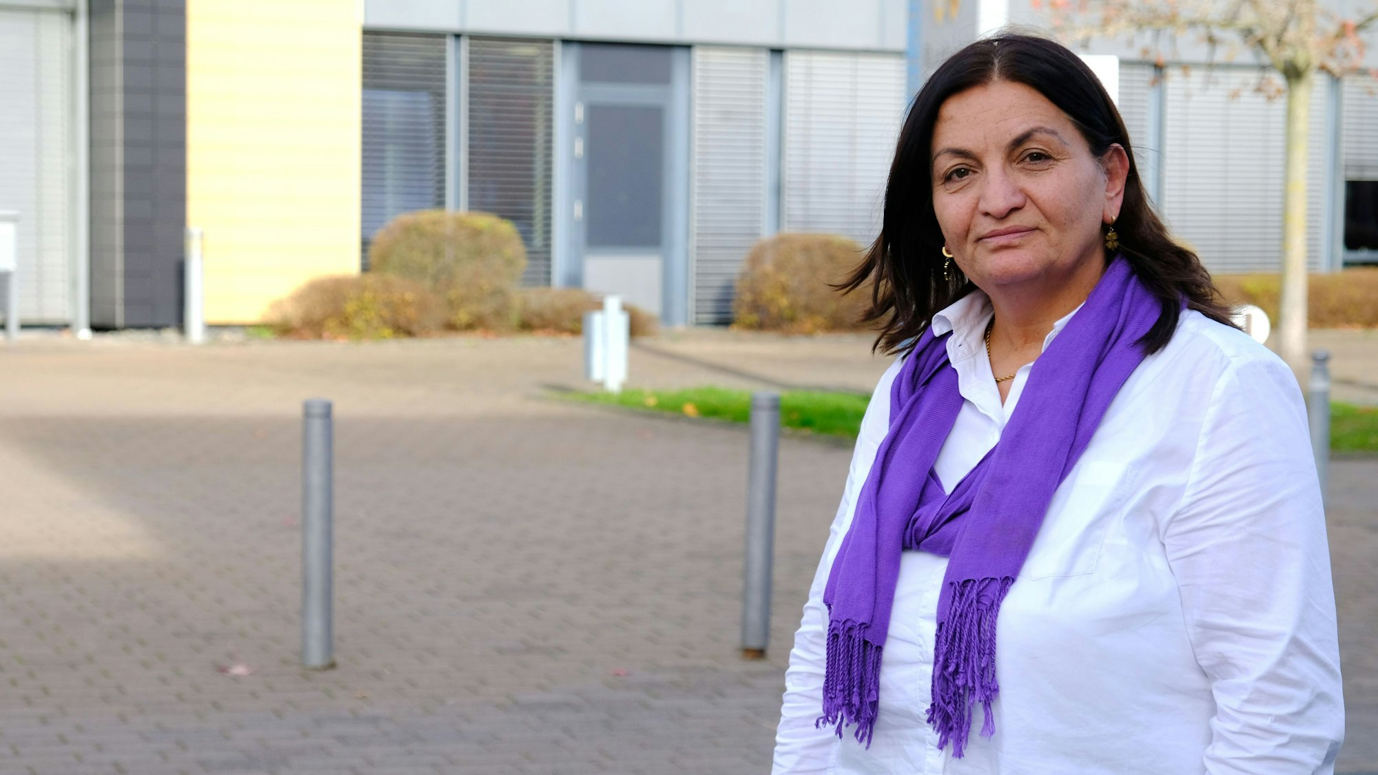 Die Mechernicher Lokalpolitikerin Zizik (genannt: Zosan) Sahbaz steht vor dem Mechernicher Rathaus. Sie trägt eine weiße Bluse und einen lilafarbenen Schal.