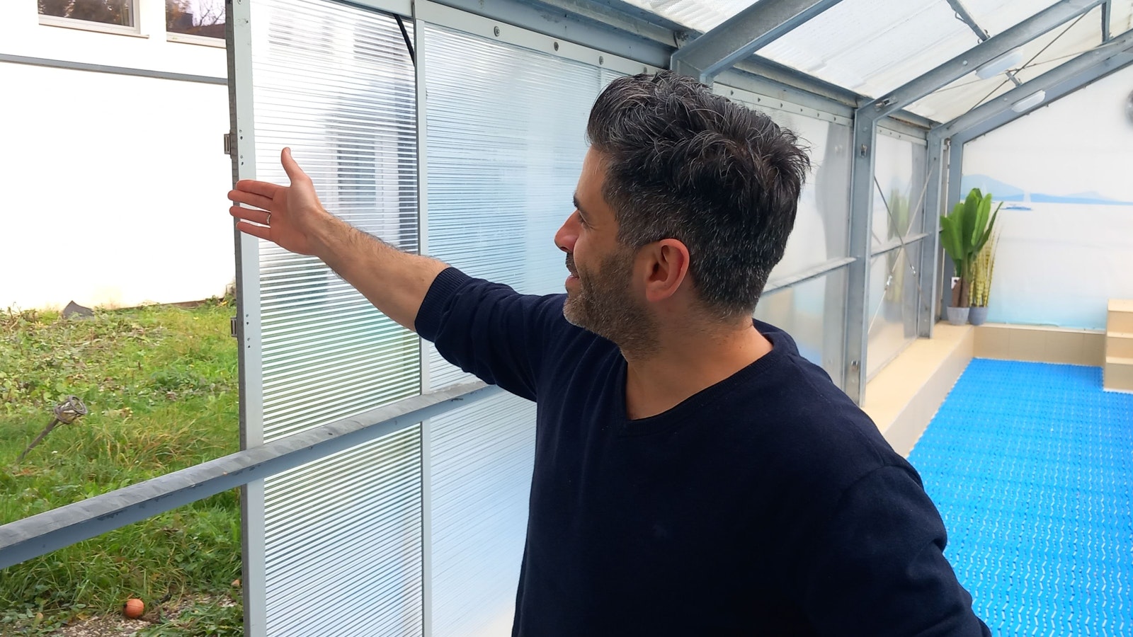 Bilal Shabib öffnet die zu dünne Einhausung aus Kunststoffplatten und gibt den Blick auf die ein Meter zu hohe Mauer zum Spielplatz- und Sportgelände nebenan frei.