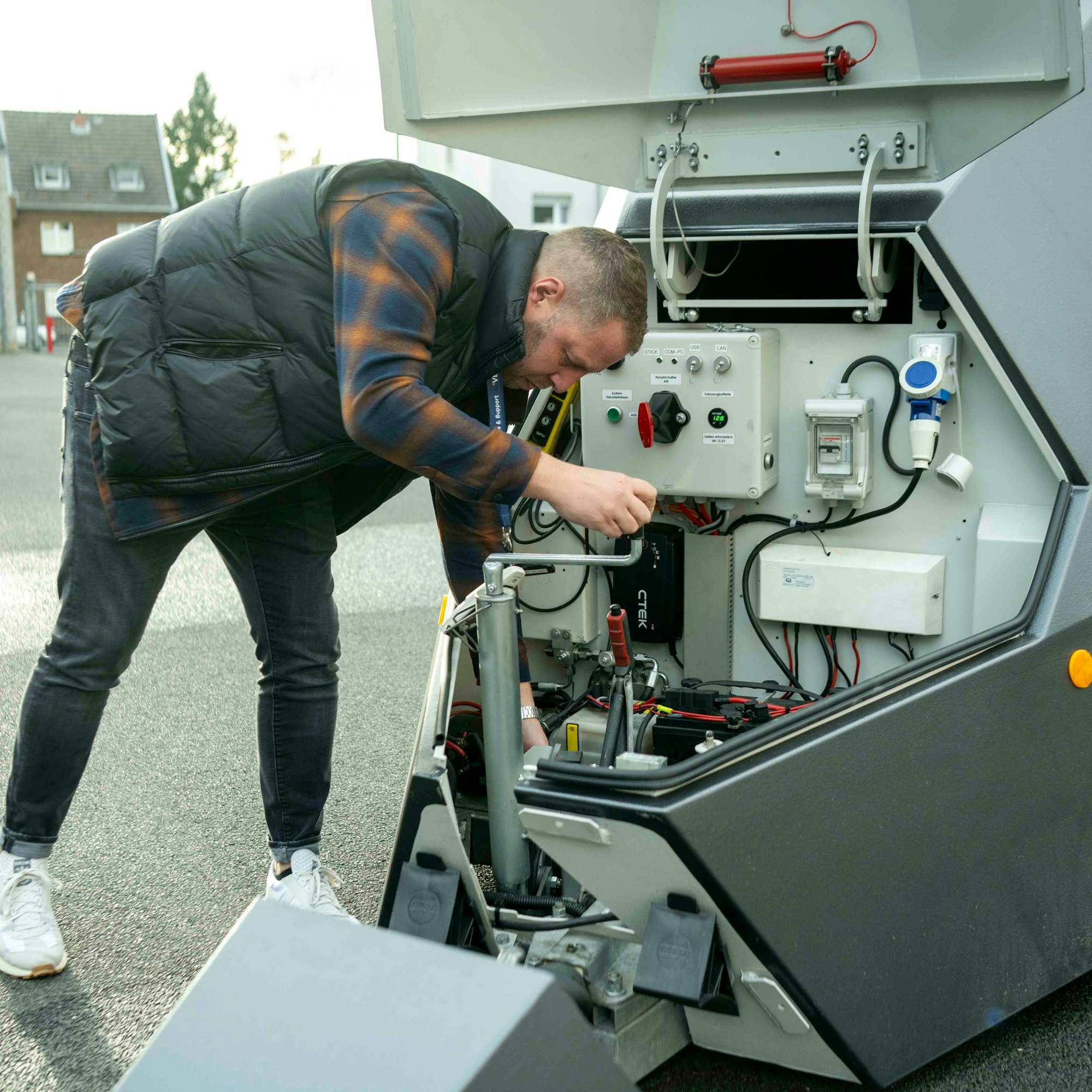 Ein Mann, der über seinem Karo-Hemd eine Steppweste trägt, bedient eine Kurbel am geöffneten Blitzer-Anhänger.