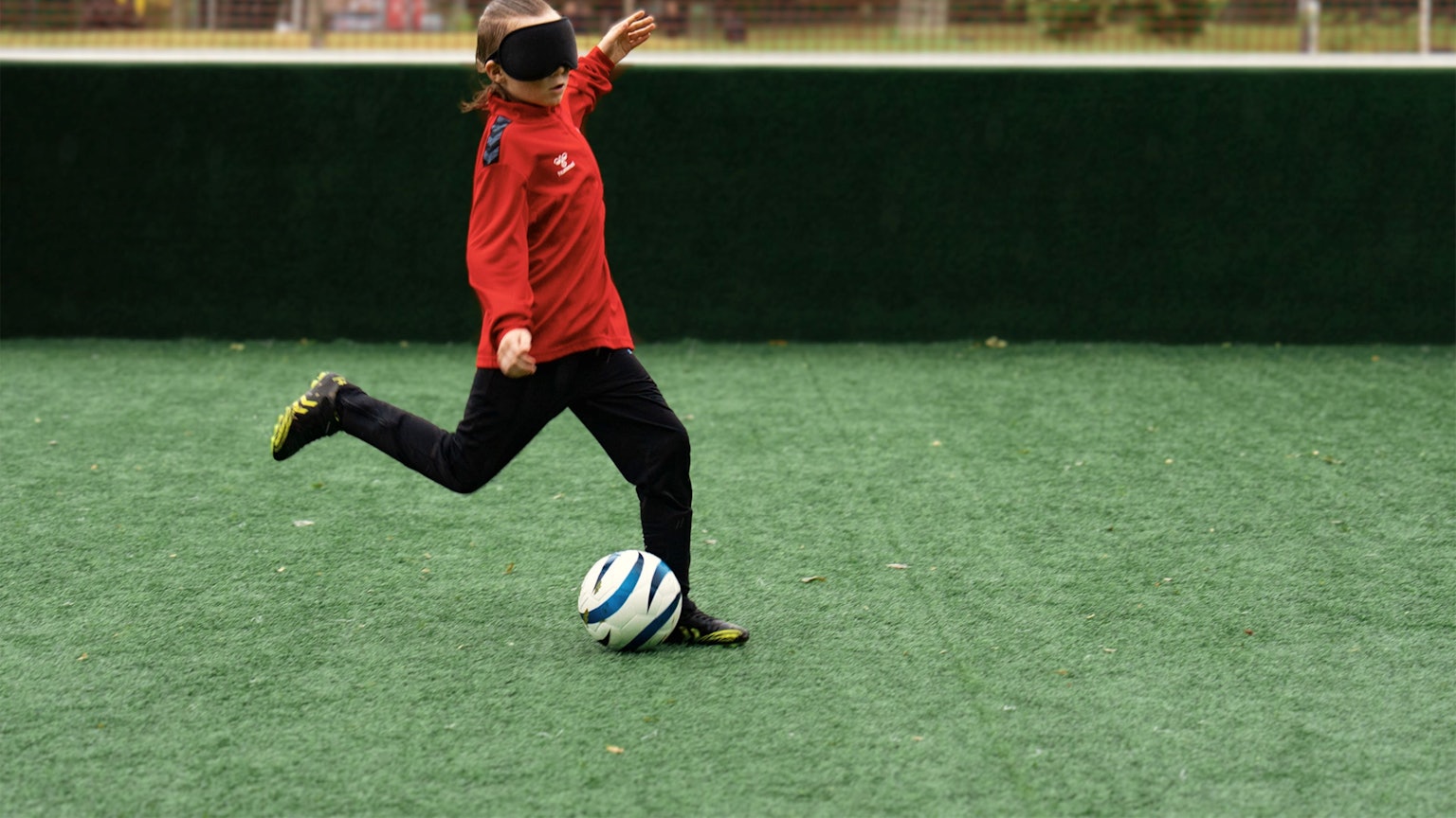 Zu sehen ist ein junger Blindenfußballer, der vor den Ball tritt.