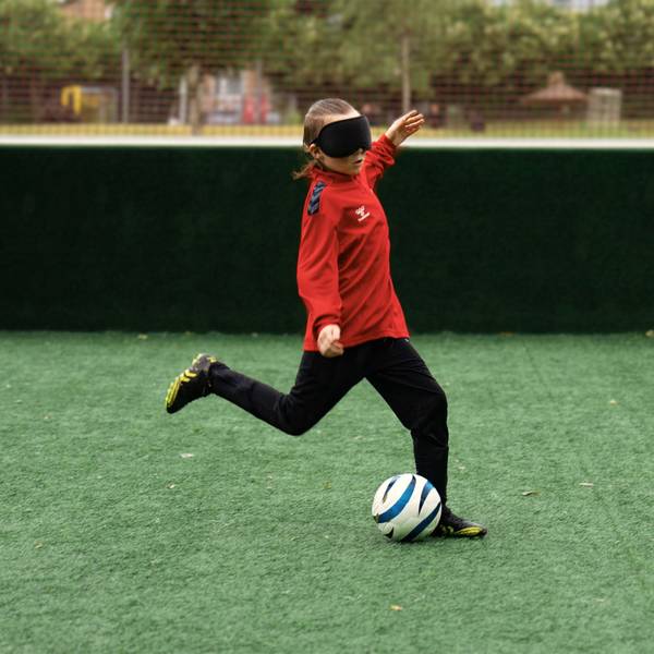 Zu sehen ist ein junger Blindenfußballer, der vor den Ball tritt.