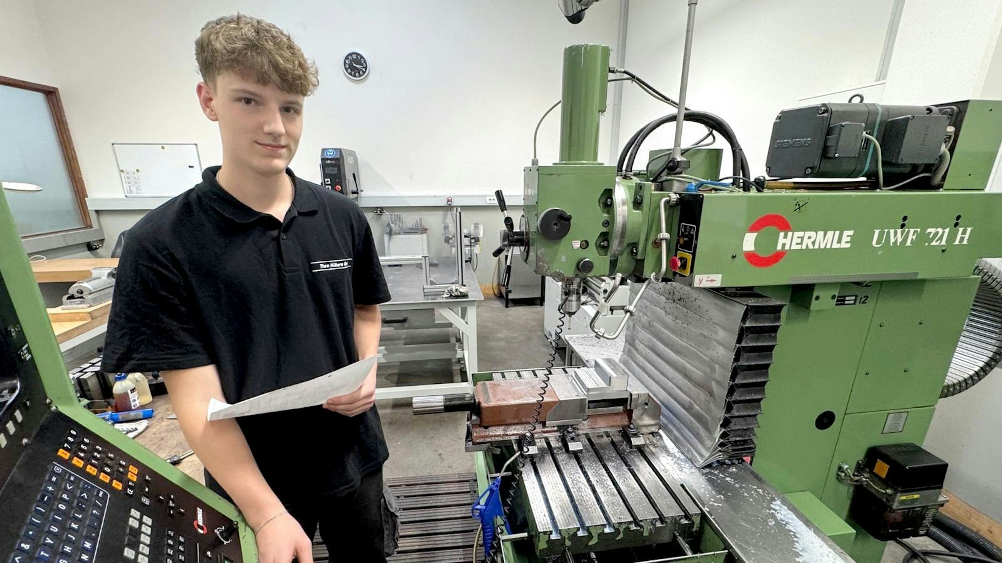 Jason Epp steht neben einer Fräsmaschine und hält ein Stück Papier in der Hand.