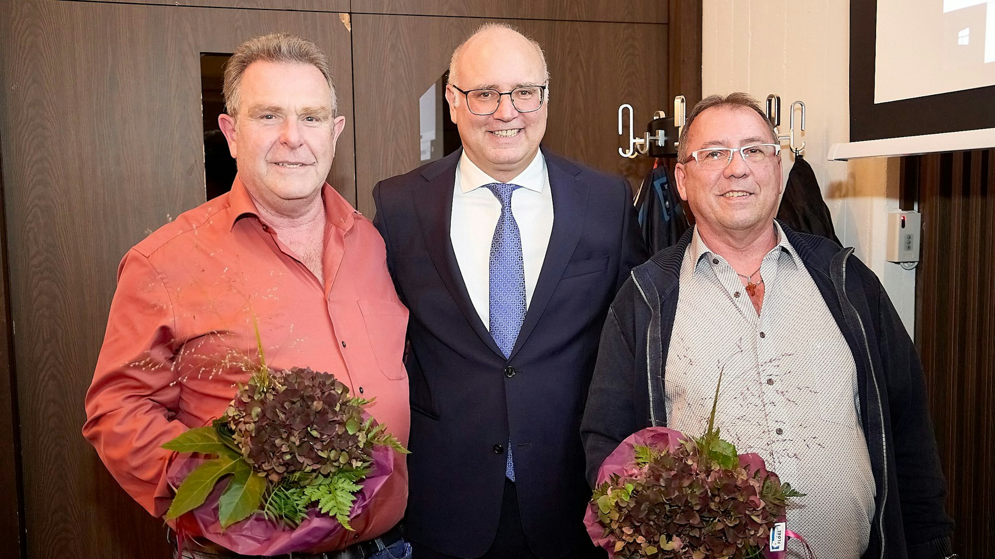 Werner Bongard, Jochen Weiler und Hans-Paul Kruppert stehen nebeneinander. Bongard und Kruppert haben jeweils einen Blumenstrauß in der Hand.