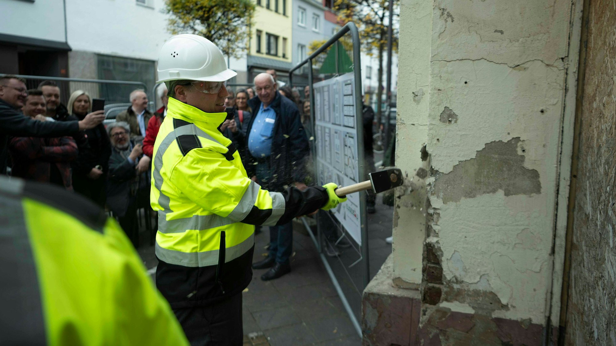 Der Euskirchener Bürgermeister Sacha Reichelt hat einen Vorschlaghammer in der Hand und schlägt damit gegen die Fassade eines Hauses, das abgerissen wird.