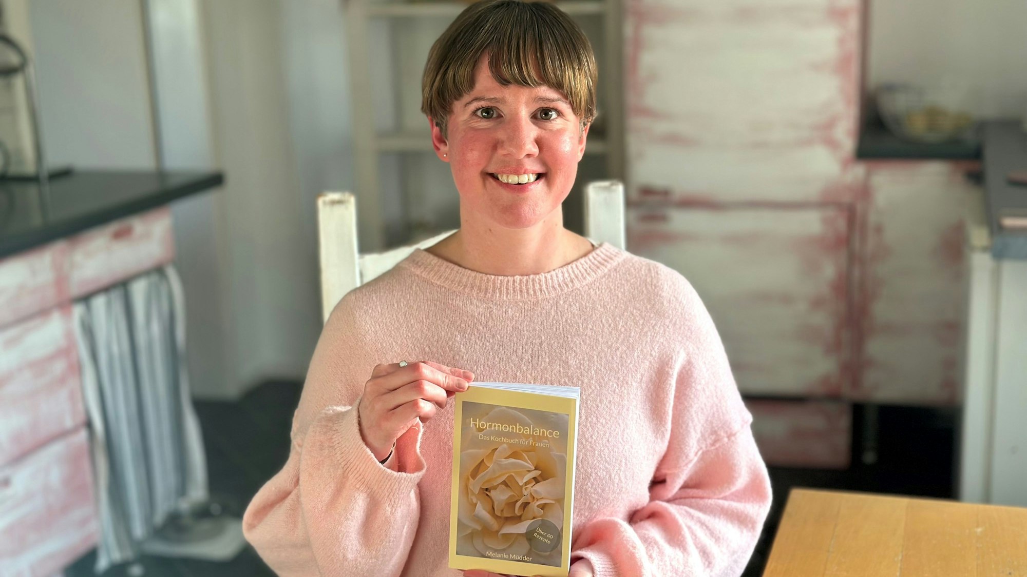 Eine Frau in einem rosafarbenen Pullover hält ein Buch.