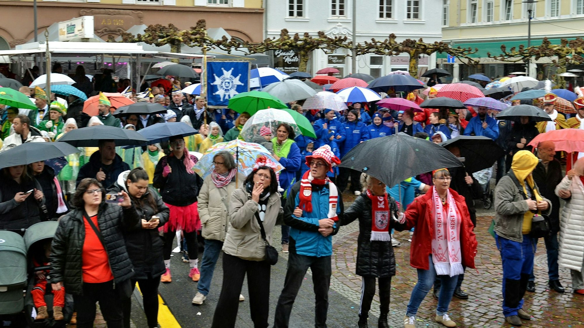 Ein Blick auf das Publikum auf dem Alten Markt. Die Jecken schützen sich mit Schirmen und Kopfbedeckungen vor dem Regen.